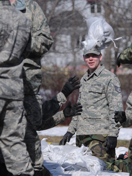 Staff Sgt. Jeremy Jedlicka, of the 119th Maintenance Squadron, smiles as he watches a sandbag fly through the air on route to the flood barrier he is helping to build March 17, Fargo, N.D.  He is working in a group of civilian volunteers and North Dakota Air National Guard personnel who are moving sandbags from pallets in front yard driveways into flood prone areas of backyards in the south Fargo neighborhood called the Timberline area along drain 27.  The drainage coulee empties into the Red River along the North Dakota and Minnesota border, but sometimes backs up into the residential neighborhoods when the river reaches major flood stages. 