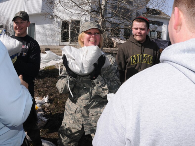 Senior Master Sgt. Susan Schroeder, of the 119th Communications Flight, smiles as she passes a sandbag along a flood barrier building  group of civilian volunteers and North Dakota Air National Guard personnel March 17, Fargo, N.D.  The mixture of civilian and military personnel are moving sandbags from pallets in front yard driveways into flood prone areas of backyards in the south Fargo neighborhood called the Timberline area along drain 27.  The drainage coulee empties into the Red River along the North Dakota and Minnesota border, but sometimes backs up into the residential neighborhoods when the river reaches major flood stages. 