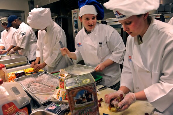 ELLSWORTH AIR FORCE BASE, S.D. -- (Center) Airmen 1st Class Steffanie Whipple and Sarah Meador, 28th Force Support Squadron food services technicians, discuss the whipped fruit dessert they’re preparing for the second annual "Ellsworth Iron Chef" competition, March 17. The teams had one hour to create an appetizer, entrée and dessert from the list of approved ingredients they were provided. (U.S. Air Force photo/Senior Airman Marc I. Lane)