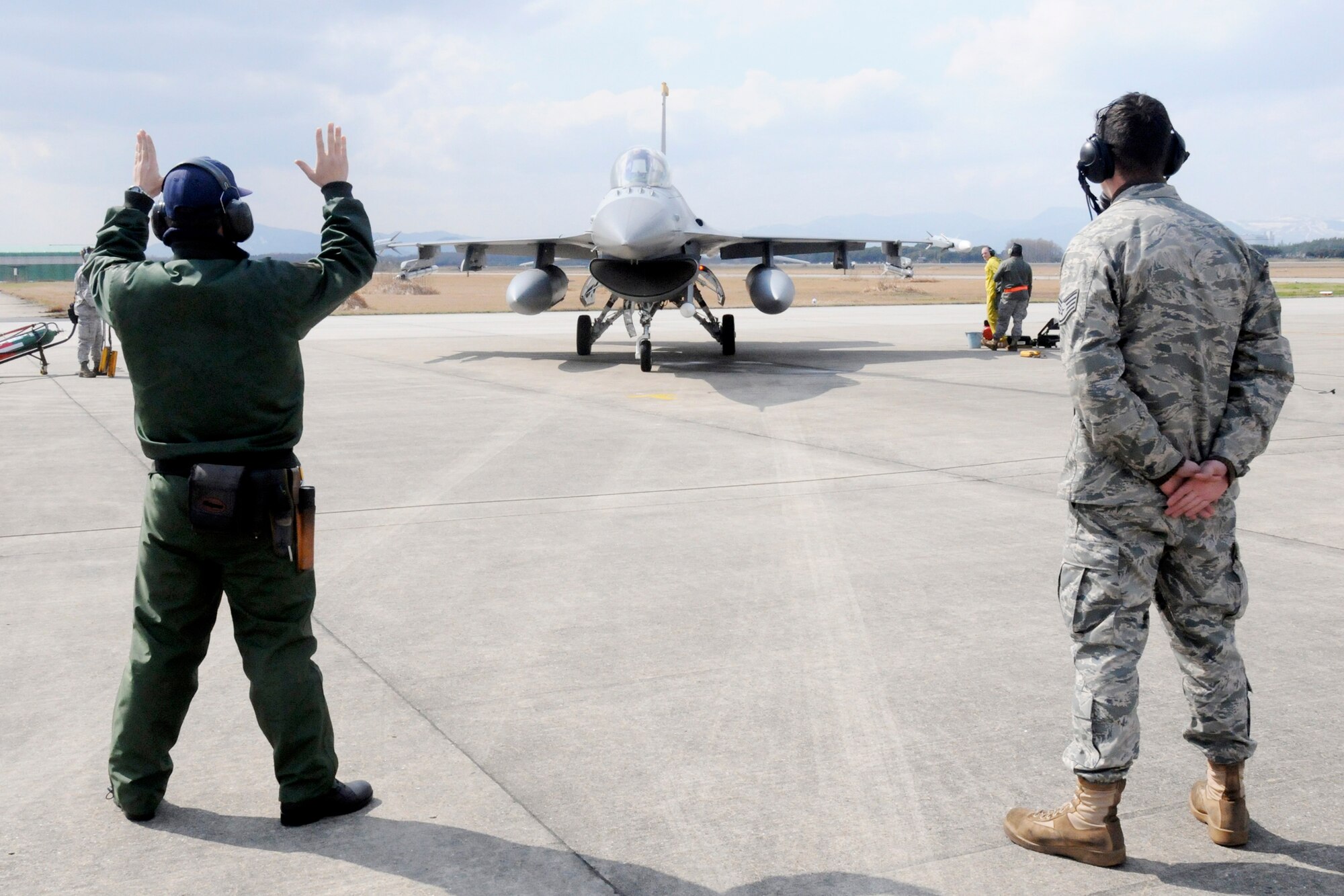 Japan Air Self Defense Force Senior Airman Naoki Yamashita marshals in an F-16 Fighting Falcon under the watch of Staff Sgt. Christopher Audet  during an aviation training relocation exercise March 11, 2010, at Tsuiki Air Base, Japan. Airman Yamashita is an F-15 crewchief. Sergeant Audet is a 35th Aircraft Maintenance Squadron crewchief. (U.S. Air Force photo/Staff Sgt. Rachel Martinez)