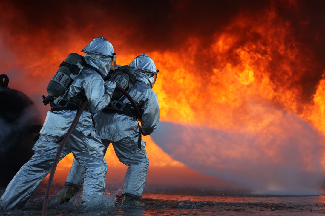 Two Marines with Marine Wing Support Squadron 271 fight the giant flames and intense heat to put out a fuel fire that was started for training purposes at the station aircraft rescue and firefighting training pit, March 19.