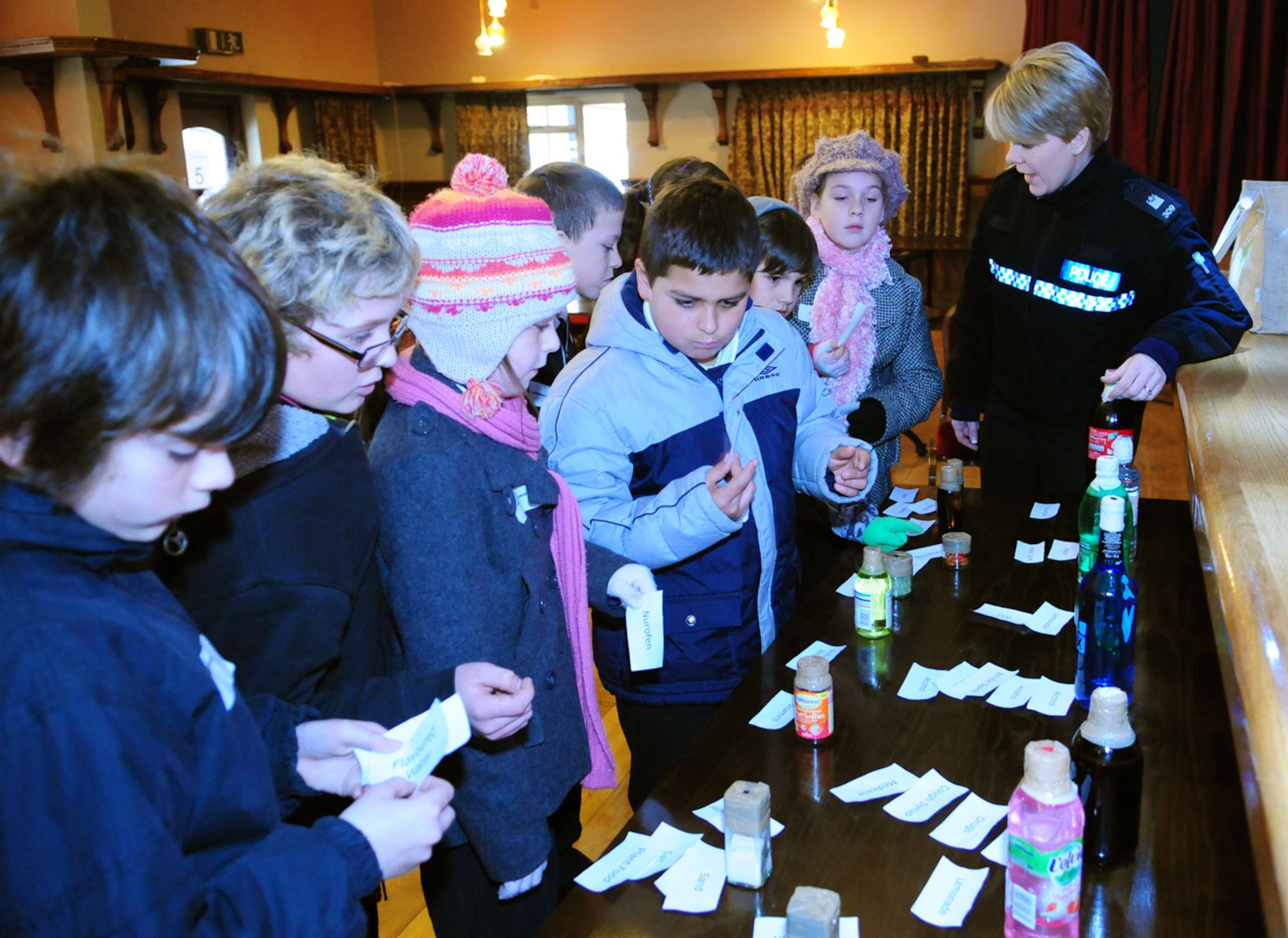 Children from Breckland Middle School, Brandon, take a look at examples of what could be dangerous substances, as Police Constable Helen Self, Mildenhall Safer Neighbourhood Team, explains exactly what the different items are. This scenario was part of the Crucial Crew experience -- a week long event for Year 5 local middle school children (including Lakenheath Intermediate School). They got to experience different scenarios which included learning about dangerous substances and prescribed medicines that can be found the home our outside, criminal damage, Internet safety and making emergency 999 calls.  (U.S. Air Force photo/Karen Abeyasekere)