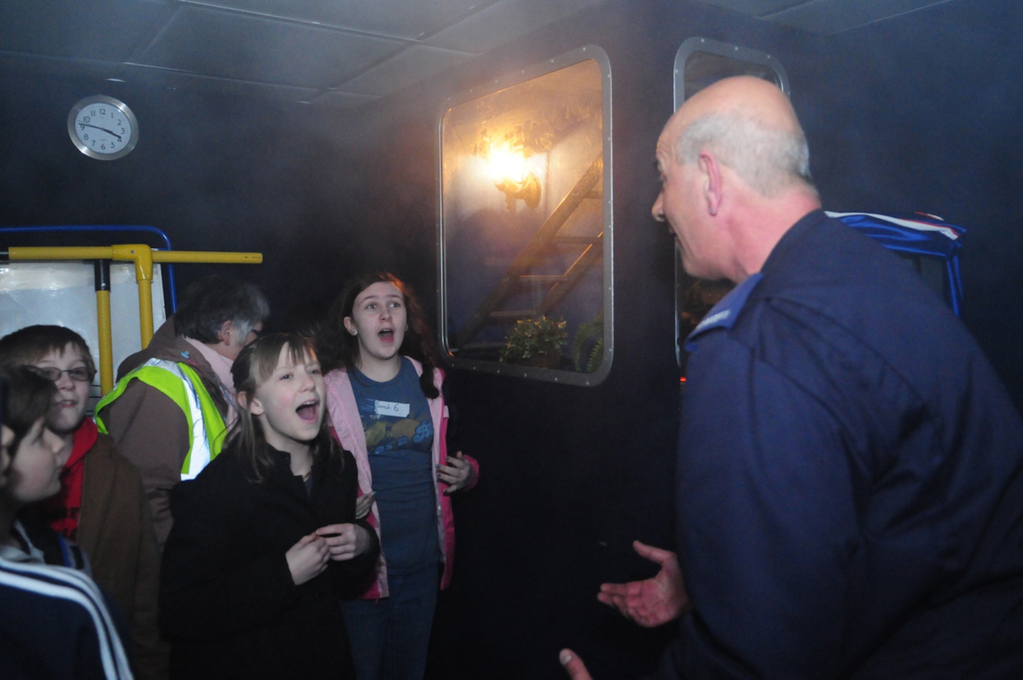 Colin Provins, right, community fire safety officer for Suffolk, tells children from Liberty Intermediate School, RAF Lakenheath, to shout as loud as possible and stamp their feet, while they were in the Fire Experience Unit. The unit showed a scenario with different fire hazards, and ended by being filled with smoke. Mr. Provins and other firefighters talked to children about the dangers of fire hazards, and what to do if they saw or were in a fire. The unit was just one of eight scenarios which were part of the Crucial Crew experience - an annual week-long event for local middle school children from several different schools. Nine volunteers from RAF Mildenhall were among the total of between 50 and 60 volunteers who helped make the event happen. (U.S. Air Force photo/Karen Abeyasekere)