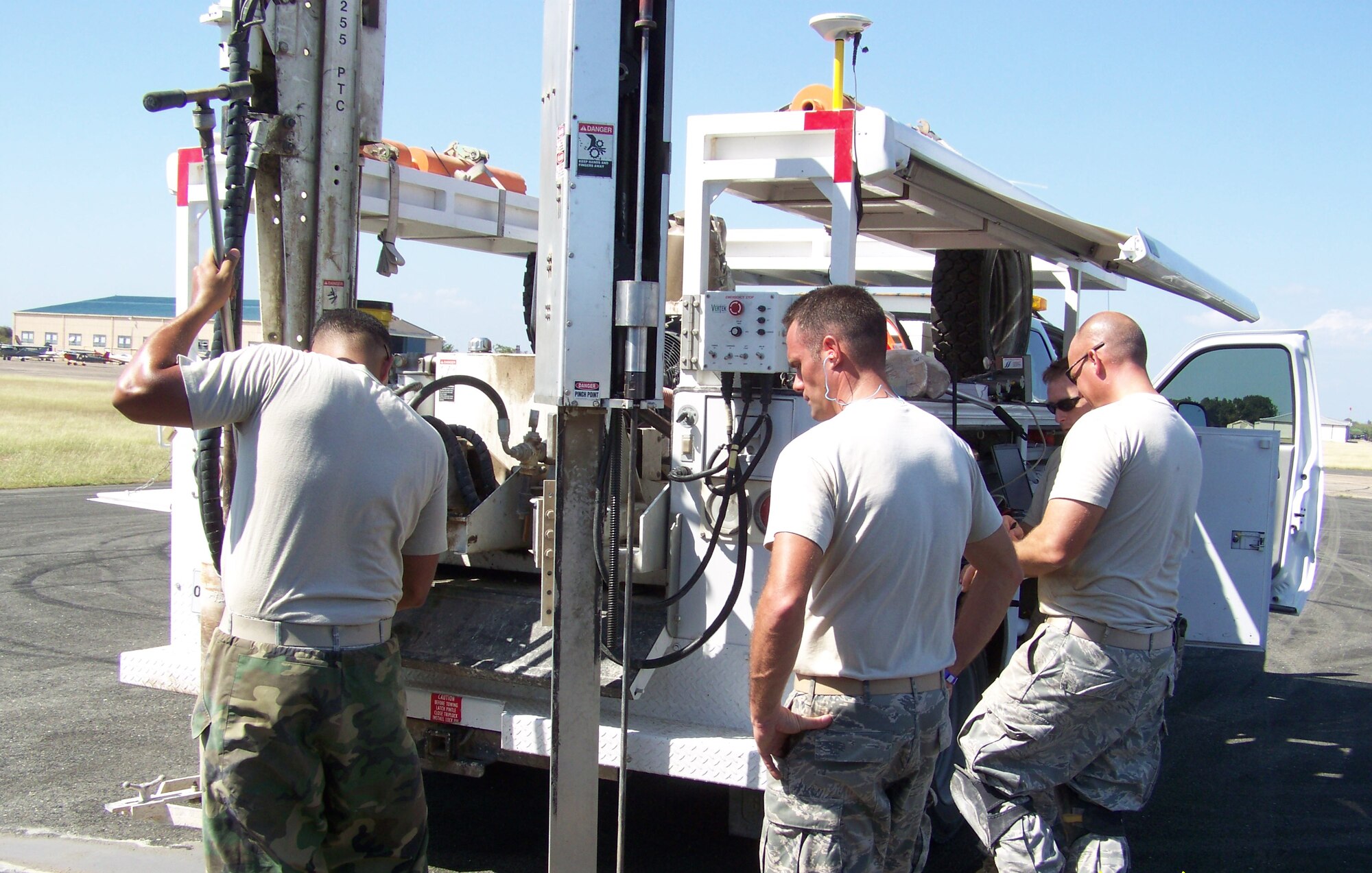 Staff Sgt. Harold Muniz, Air Force Civil Engineer Support Agency, drills into the tarmac of the Port-au-Prince  runway to conduct strength tests on it in early February. Tech. Sgt. Chad Lepley, 819th RED HORSE Squadron, looks on, while two other team members read guages in the specialized vehicle. A seven person team, three from AFCESA and four from the 819th RHS, spent 30 days in the country collecting samples to evaluate and report on. (U.S. Air Force courtesy photo)