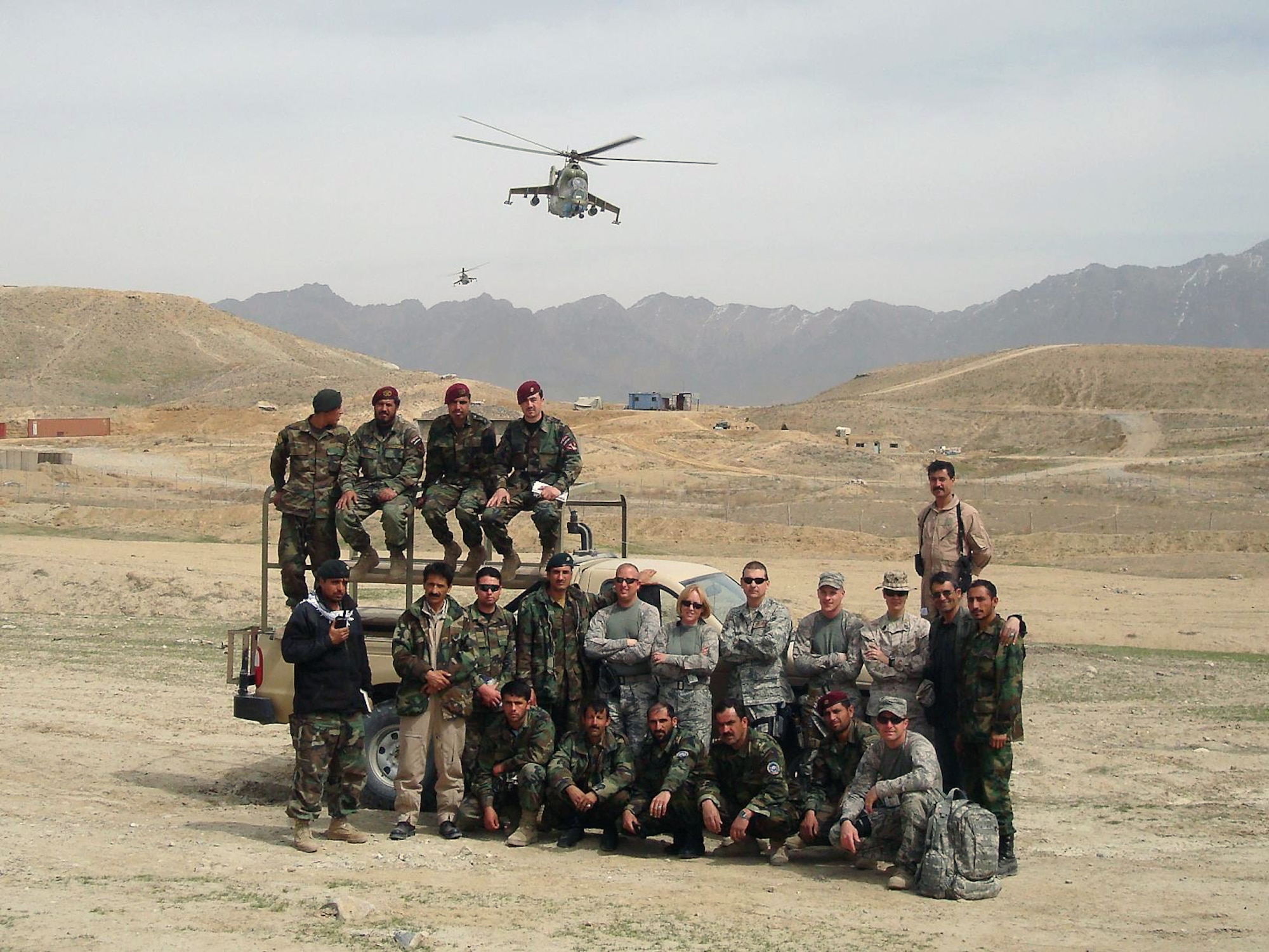 U.S. Air Force Airmen from the 438th Air Expeditionary Advisory Group pose for a photo with members of the Afghan National Army Corps as Afghan MI-35 gunships fly overhead in Afghanistan. The U.S. Airmen are currently training Afghan airmen to be forward observers, the eyes and ears on the ground for Afghan pilots in cockpits of MI-35 helicopters. According to Brig. Gen. Michael Boera, 438th Air Expeditionary Wing commander, Afghan pilots are familiar and comfortable with the Mi-35 helicopter, an airframe well-suited to Afghanistan.  (Courtesy photo)            