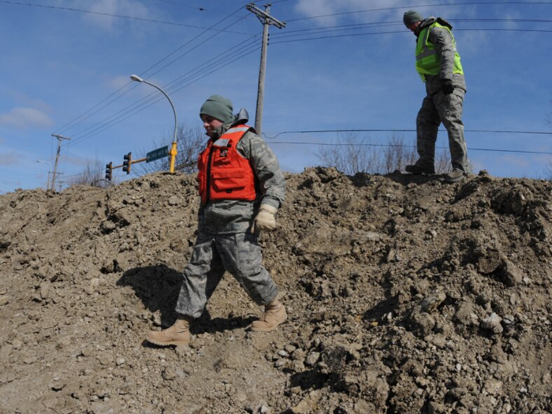 Senior Airman Jeremiah Colbert, of the 119th Maintenance Squadron, left, and Staff Sgt. Joshua Hahn, of the 119th Logistics Readiness Squadron, climb down off of a flood dike March 19, along the Red River in downtown Fargo, N.D.  The pair of North Dakota Air National Guard members are tasked with keeping sightseers off of the flood dikes and also to monitor the clay dikes for possible trouble spots that could become breaches in the dike if they are left unchecked.  (DoD photo by Senior Master Sgt. David H. Lipp) (Released)
