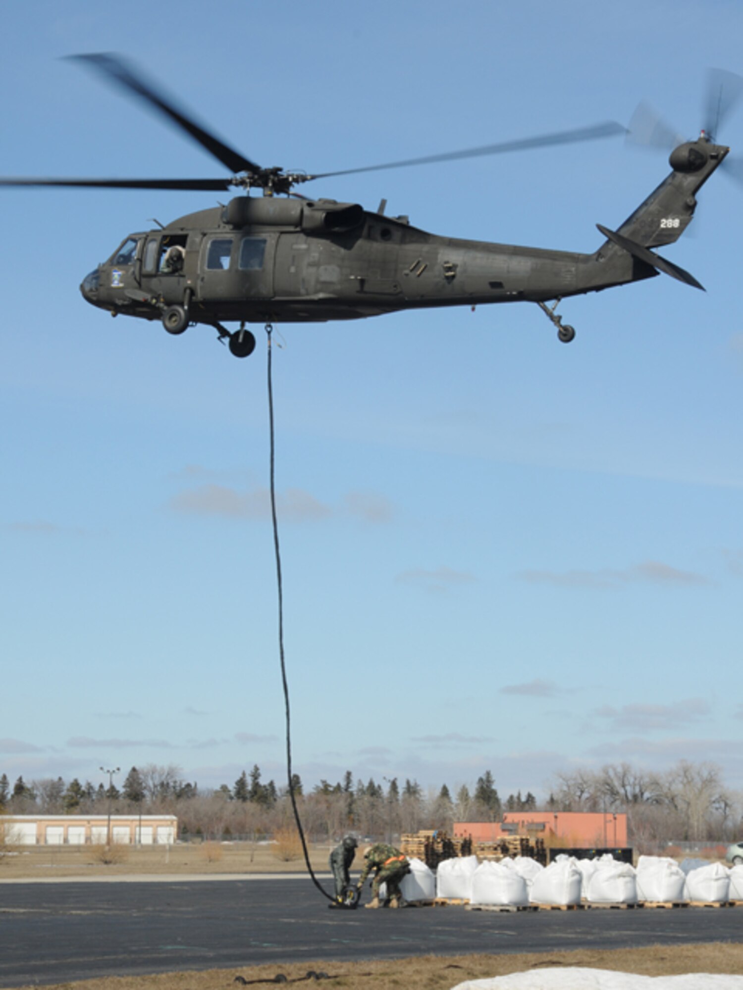 A Minnesota Army National Guard UH-60 Blackhawk helicopter practices sling load operations March 19, Fargo, N.D.   Sgt. 1st Class Todd Suderheimer, of the 2/147th Aviation Battalion, trains North Dakota Air National Guard members on the ground how to link a 1.5 ton sandbag unto the helicopter cable so that the sandbag can be transported to a simulated flood fighting location. The training and placement of the large sandbags are in preparation for UH-60 helicopter sling-load flood operations, should they be necessary in an emergency situation with rising flood waters anywhere in eastern North Dakota.