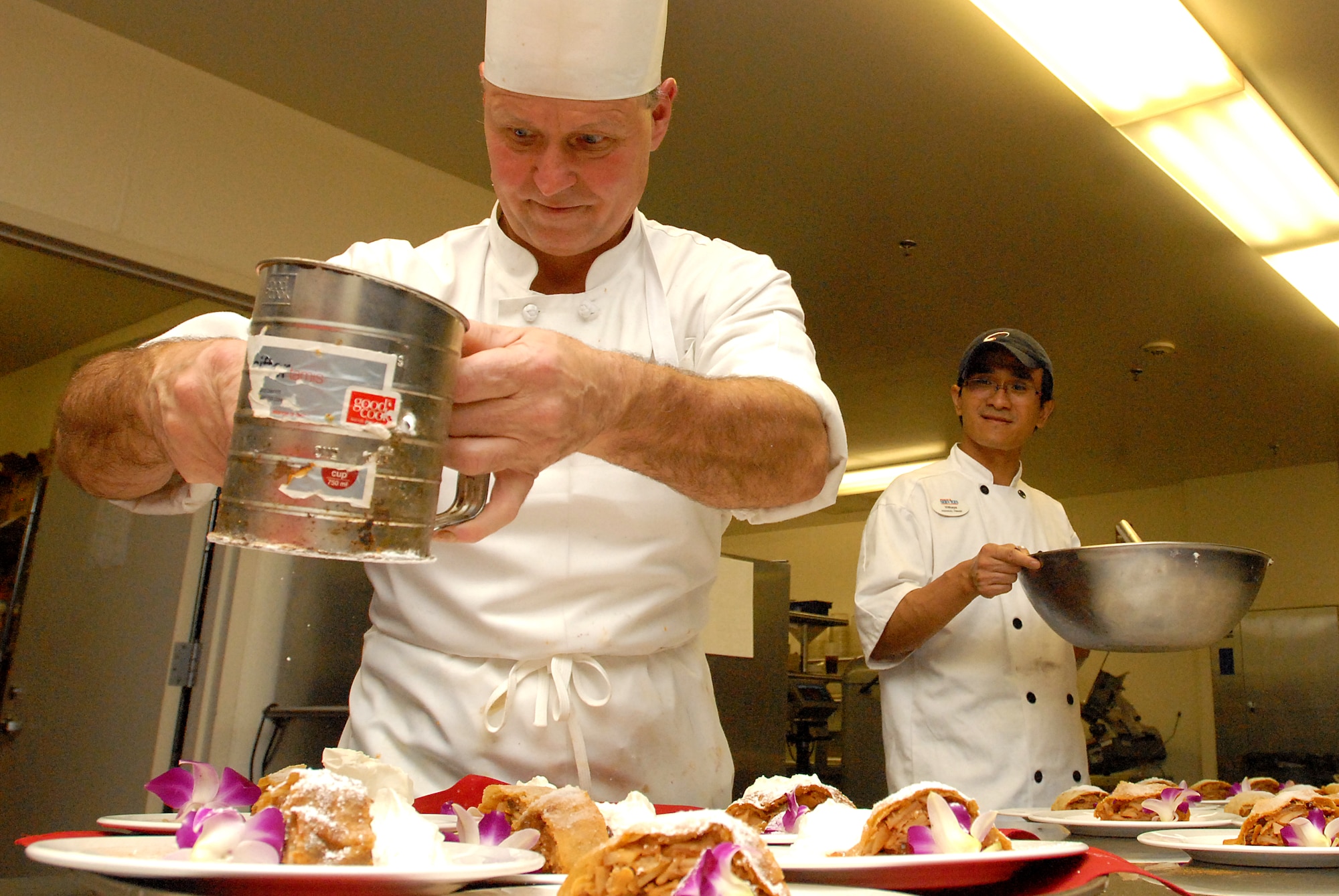 JOINT BASE PEARL HARBOR HICKAM, Hawaii -- Chef Andreas Knapp, Tradewinds Enlisted Club executive chef, sprinkles powdered sugar on apple strudels during the sixth course of a Hungarian themed meal for the Gourmet Club at the Tradewinds Enlisted Club March 15. Twenty-seven members enjoyed Hungarian fair for the six course meal, prepared in the traditional manner. During the reception mushroom cups with green beans, goat cheese in tartlets topped with strawberries were served as appetizers. The meal featured marinated river trout with coriander roasted bell pepper vinaigrette, goulash soup, chicken placsinta, a wild boar roast, mushroom ragout, red wine cabbage and bread dumplings, Hungarian cheese in sweet bell pepper, apple strudel with vanilla scented whipping cream for dessert. The April theme, "Springtime in Paris," will feature traditional French bistro cuisine. (U.S. Air Force photos/Staff Sgt. Mike Meares)  