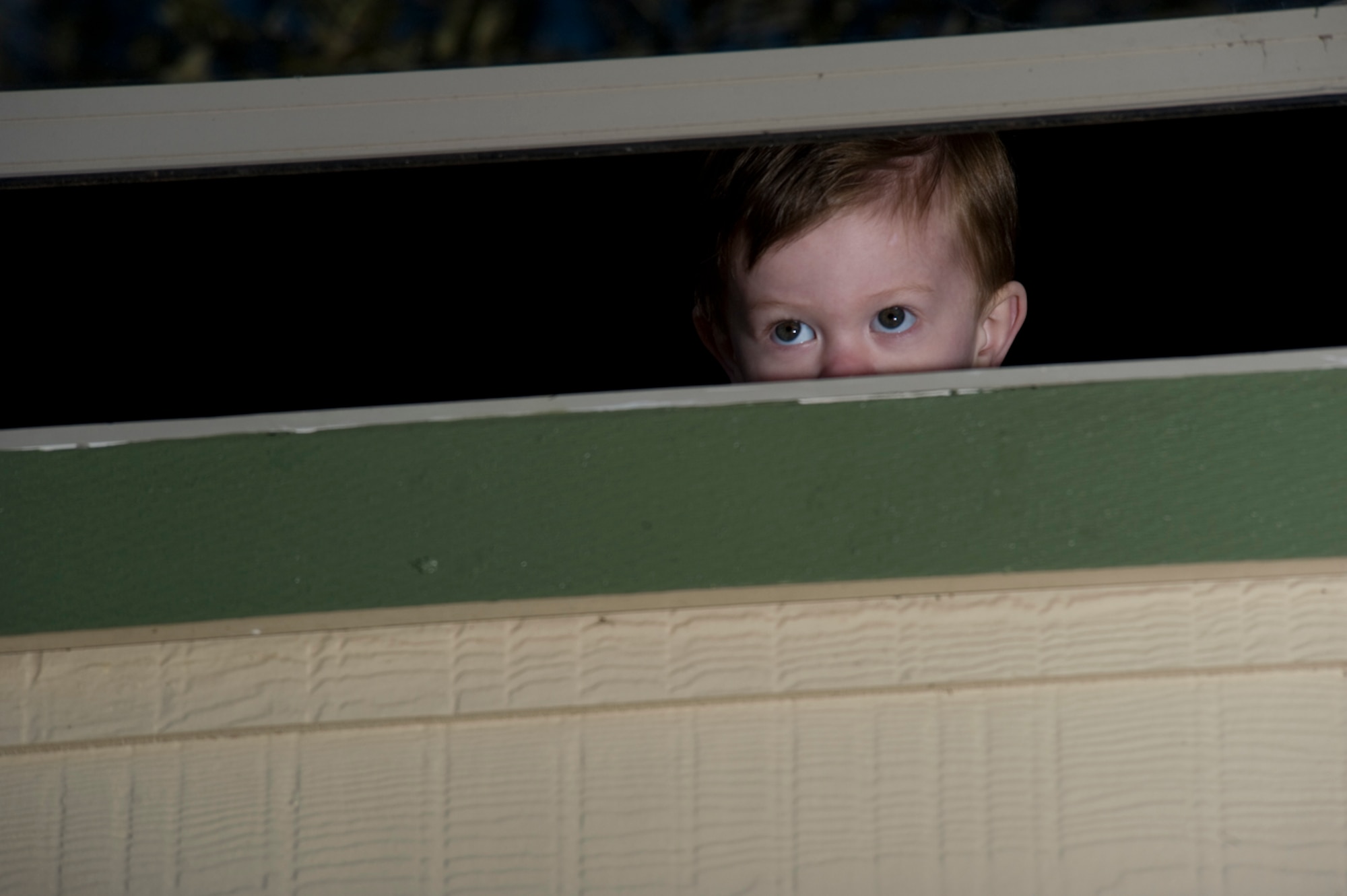 Two year-old, Cannon Jamison, peers out the second story window from which he fell 17 feet. Thankfully, 14-year-old Cary Clevenger caught him before he hit the concrete driveway.
(Photo by TSgt Samuel Bendet)