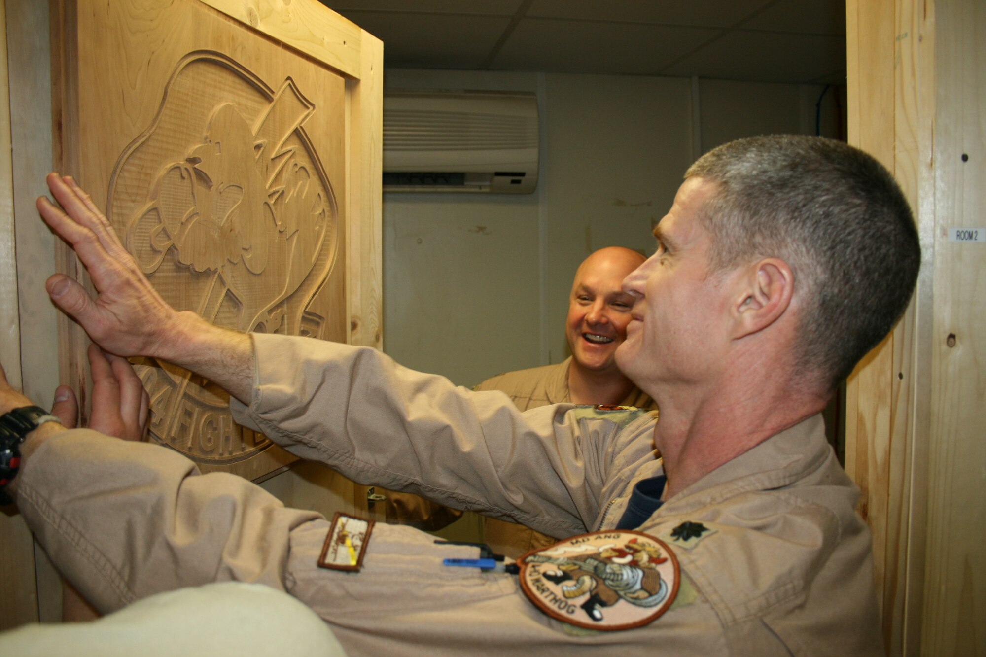 Lt. Col. Paul Johnson mounts a wooden likeness of the 104th Expeditionary Fighter Squadron insignia, an oriole with a lightning bolt, on the squadron commander's door at Kandahar Airfield, Afghanistan, as Lt. Col. Patrick McAlister, the squadron commander, background, admires the sign. Colonels Johnson and McAlister are deployed from the Maryland Air National Guard to the 451st Air Expeditionary Wing to support Operation Enduring Freedom. (U.S. Air Force photo by Tech. Sgt. David Speicher/Released)