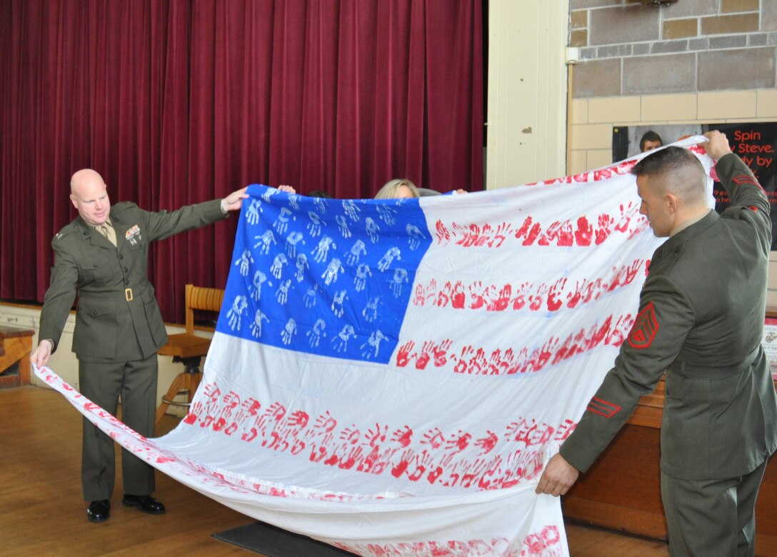 Capt. Christopher Hermann, left, and Staff Sgt. Andrew Galonzka, with Marine Wing Support Squadron 472, unfurl a special American flag at Bowie Elementary School March 18. The Bowie students created the flag from their handprints last year. The Westover Marines also presented a framed certificate of Appreciation and a letter stating when and where the flag was displayed during their unit's deployments to Iraq. (US Air Force photo/Tech. Sgt. Brian Boynton)
