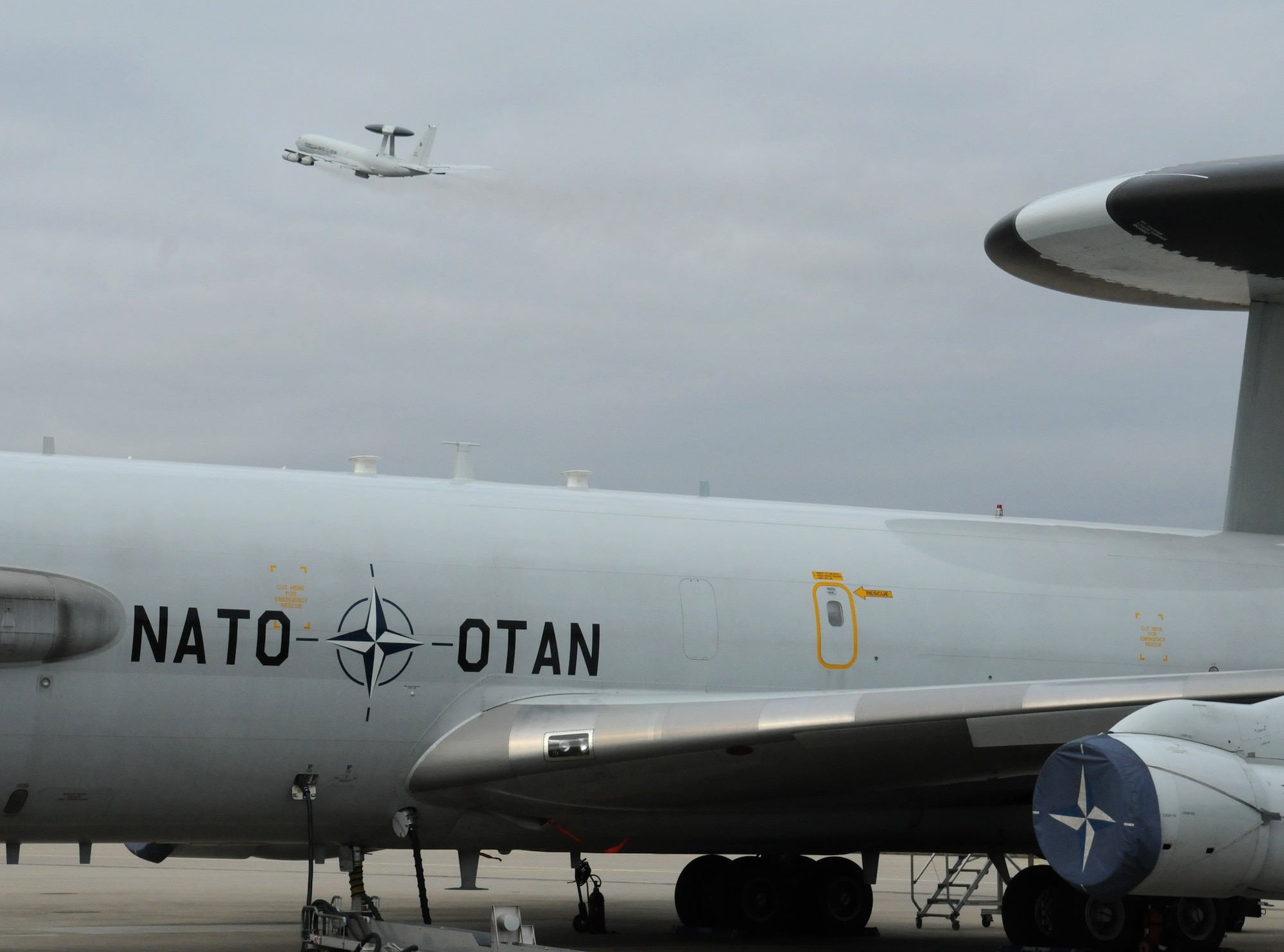 NATO AIR BASE GEILENKIRCHEN, Germany – A NATO E-3A Sentry from the NATO E-3A Airborne Early Warning and Control force component sits on the flightline after a mission as another E-3A takes off March 19. The E-3A is a four-engine, modified Boeing 707-320 aircraft that provides all-weather surveillance, command, control and communications needed by the commanders of NATO air forces. (U.S. Air Force photo/Senior Airman Nathanael Callon)