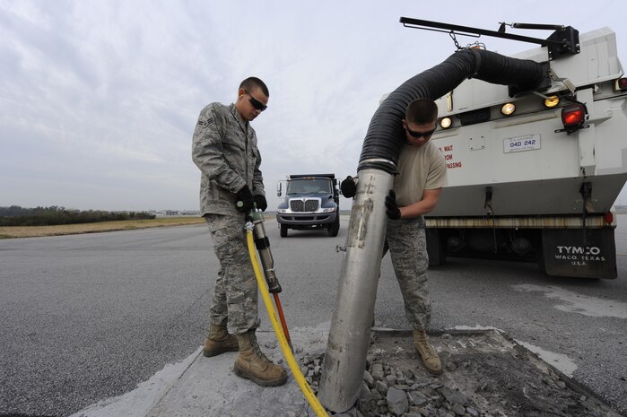 U.S. Air Force Airman 1st Class Jerry Cook uses a jack hammer to break up defective pavement on the runway while Airman 1st Class Michael Childers uses a street sweeper vacuum to suck up the debris so it can be replaced with asphalt at Joint Base Charleston, S.C., March 25, 2010. Base civil engineers have monthly runway closures to repair discrepancies as well as on an as-need basis. Airmen Cook and Childers are pavements and equipment journeymen with the 628th Civil Engineer Squadron. (U.S. Air Force photo by James M. Bowman/released)