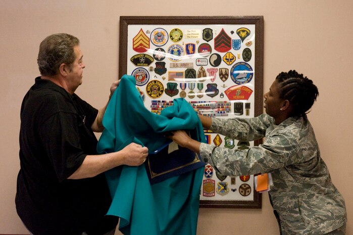 NELLIS AIR FORCE BASE, NEV.-- Andre Harper and 2nd Lt. Taveya Murphy unveil a collage which was presented at Mike O' Callahan Federal Hospital March 19 in order to recognize all veterans and active duty servicemembers of the United States military. Mr. Harper's group, Patches, creates collages for military members, children's hospitals and other organizations. All of the work done by Patches is made possible through donations, which usually come from veterans and their families. (U.S. Air Force Photo / Airman 1st Class Jamie Nicley)