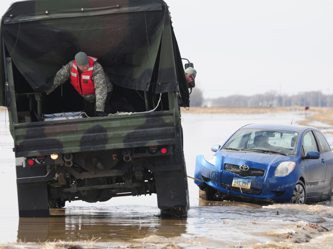 Spc. Jeremy Kasperson sits in the rear of a North Dakota National Guard truck as he gives directions for backing out of a washed out road March 25 in rural Cass County. The truck is towing a stranded automobile from the washed out roadway. Cass County Tactical Operations Center liaison officer Capt. Grant Larson, of the 119th Maintenance Squadron, North Dakota Air National Guard, can be seen giving guidance from the cab of the truck. Kasperson is a member of the 815th Engineer Company’s North Dakota National Guard quick response force (QRF) team that is being called to the scene by the Cass County Sherriff’s Department to assist with the vehicle recovery. The driver of the vehicle was able to get clear of the car and make his way through the freezing water to safety before help arrived. (DoD photo by Senior Master Sgt. David H. Lipp) (Released)
