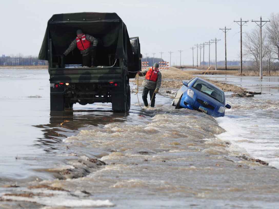 Sgt. Preston Steele attaches a towing chain to a partially submerged vehicle March 25 on a washed out portion of a gravel road a few miles west of Harwood, N.D., as Spc. Jeremy Kasperson gives directions from the rear for backing the truck. Steele and Kasperson are both in the 815th Engineer Company’s North Dakota National Guard quick response force (QRF) team that is being called to the scene by the Cass County Sherriff’s Department to assist with the vehicle recovery. The driver of the vehicle was able to get clear of the car and make his way through the freezing water to safety before help arrived.  (DoD photo by Senior Master Sgt. David H. Lipp) (Released)


