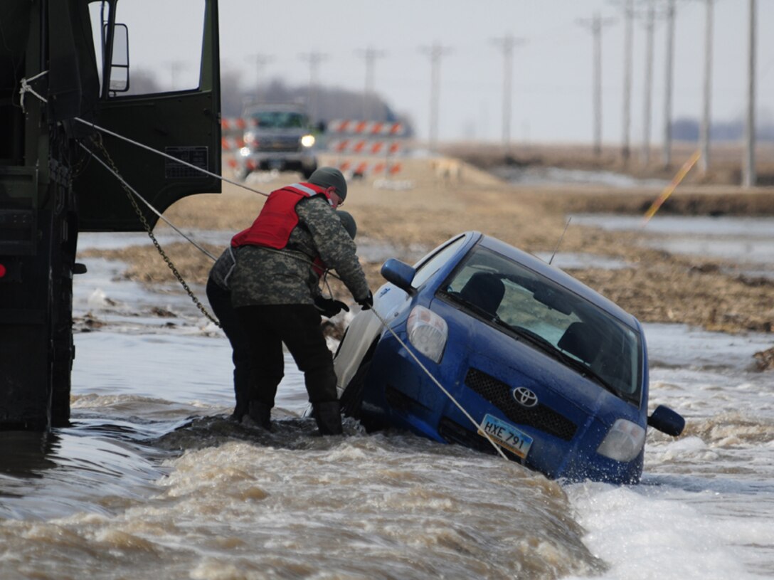 Sgt. Preston Steele and Spc. Jeremy Kasperson, both of the 815th Engineer Company, attach a towing chain to a partially submerged vehicle March 25 on a washed out portion of a gravel road a few miles west of Harwood, N.D.  Steele and Kasperson are members of a North Dakota National Guard quick response force (QRF) team that is being called to the scene by the Cass County Sherriff’s Department to assist with the vehicle recovery.  The driver of the vehicle was able to get clear of the car and make his way through the freezing water to safety before help arrived.  (DoD photo by Senior Master Sgt. David H. Lipp) (Released)
