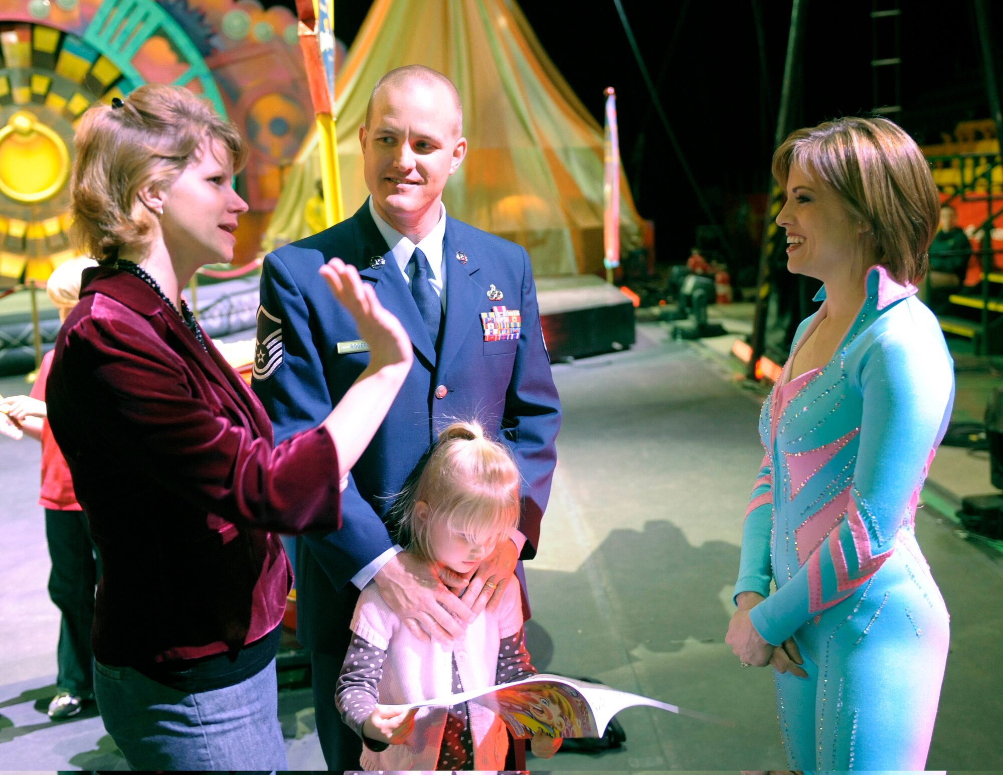 Air Force Master Sgt. Cameron Rogers (second from left) looks on as his wife Maggie (left) talks with circus human cannon ball and former Air Force Reservist Tina Miser (right) prior to the start of the Ringling Bros. and Barnum & Bailey "Zing Zang Zoom" circus performance at George Mason University's Patriot Center March 26, 2010, Fairfax, Va. Sergeant Rogers’ 5-year-old daughter Laine is checking out the program. Sergeant Rogers and his family served as guest ringmasters for the circus performance.  Sergeant Rogers recently returned from a year-long deployment to Afghanistan and currently is the Air Force District of Washington's UH-1N helicopter program manager at Bolling Air Force Base, Washington. The Rogers family was asked to serve as guest circus ringmasters representing military families worldwide in observance of Year of the Air Force Family. (U.S. Air Force photo/Jim Varhegyi)