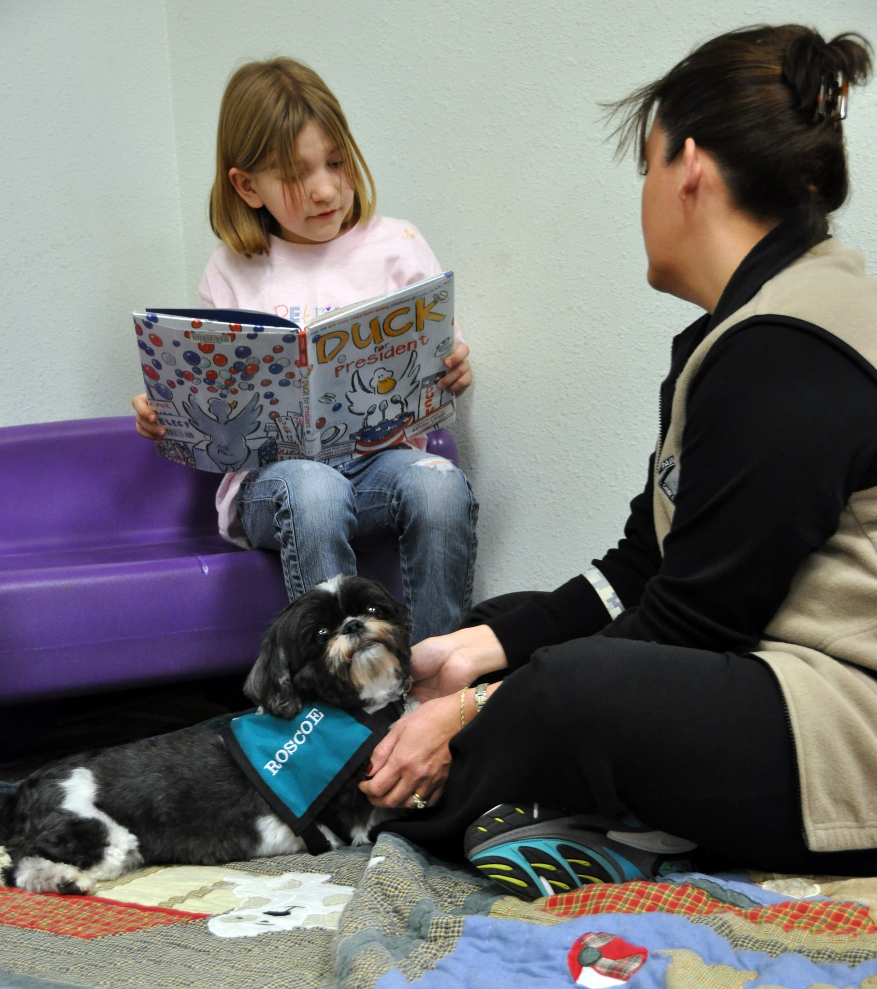 Sierra Ferren reads a book during the Paws for Reading program at the Mitchell Memorial March 11 while Roscoe the dog sits nearby. (U.S. Air Force photo/Airman Michael Battles)