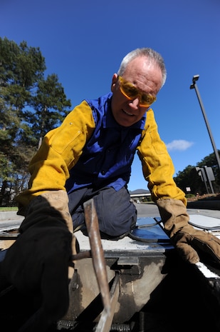 U.S. Air Force Master Sgt. Daniel Martin removes a slag, which is the residue leftover after welding, from the  pop-up security barrier at the inbound Rivers Avenue gate entrance using a chipping hammer on Joint Base Charleston, S.C., March 23, 2010. Sergeant Martin was at the gate to weld more steel to the barrier for reinforcement. Sergeant Martin is the NCO in charge of the structure shop with 628th Civil Engineer Squadron. (U.S. Air Force photo/James Bowman/released)