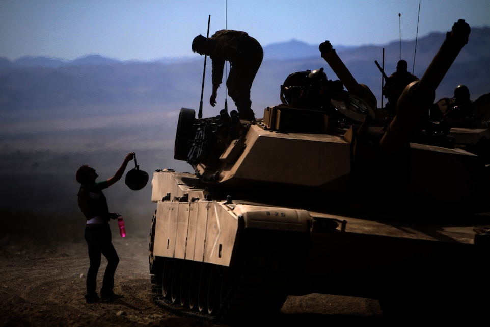 Cpl. Francisco Guzman, a tank commander with Company B, 1st Tank Battalion, retrieves his Kevlar helmet from Jessica Plummer, the wife of Lance Cpl. Chad Plummer, a crewman with Co. B, after a ride in an M1A1 Abrams Main Battle Tank during the battalion's "Jane Wayne Day" at Combat Center Range 500 March 30. The ladies also had the opportunity to fire weapons and climb aboard various tactical vehicles.