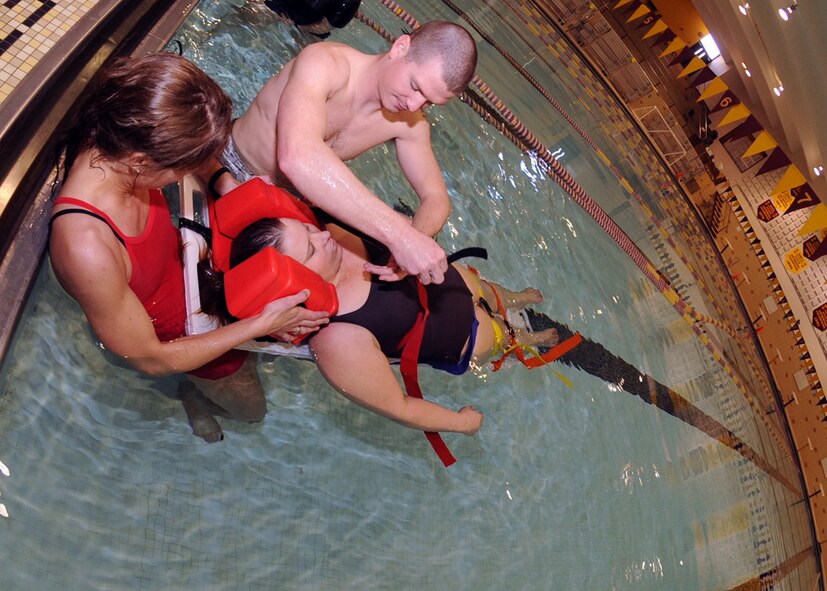 MINOT, N.D. – Capt. Tara Hasbrouck (right), 91st Operations Support Squadron ICBM weapons and tactics instructor, and (redacted), 5th Maintenance Operations Squadron aircrew ground equipment scheduler, use a backboard to rescue DeAnn Wege, 5th Force Support Squadron aquatics director and “simulated victim”, during lifeguard training at the Minot High School Magic City Campus March 27. The 3-day lifeguard training course, taught by Rachel Filkins, 5th Force Support Squadron outdoor recreation manager, involved cardiopulmonary resuscitation (CPR) and various swimming and rescue techniques. (U.S. Air Force photo by Senior Airman Sharida Jackson)