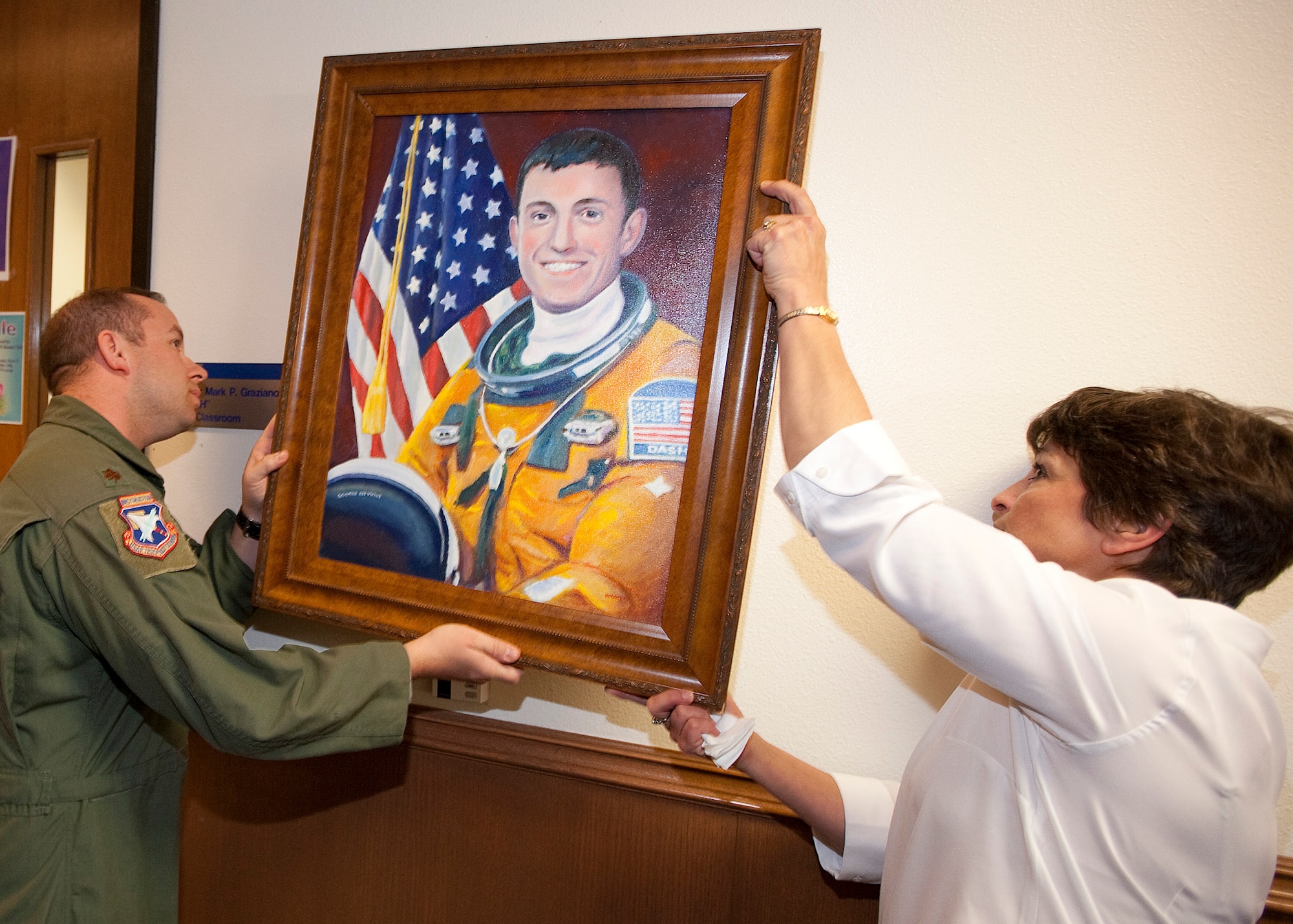 Maj. Jeffrey Kennedy, USAF TPS branch chief, systems and F-16 instructor pilot, helps Helen Graziano hang a portrait of her son, Maj. Mark "Dash" Graziano, in front of the entrance to TPS Alpha classroom.  The classroom was dedicated to Major Graziano, who died March 21, 2009 when his T-38A Talon crashed during a flight-test mission. 
