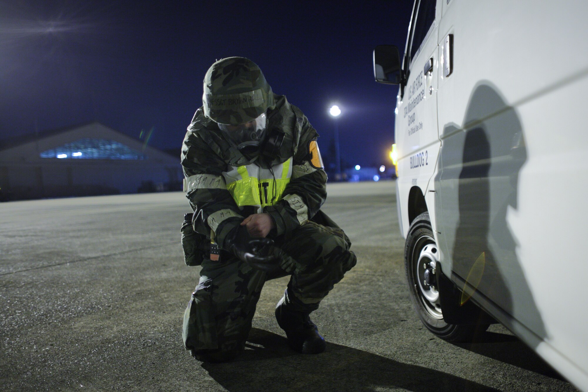 Seeking shelter besides a vehicle, Staff Sgt. Bryan Hill, 374th Maintenance Group, dons his gloves during an exercise scenario here Mar. 31. The exercise tested Yokota Airmen's operational readiness preparedness. (U.S. Air Force photo/Osakabe Yasuo)