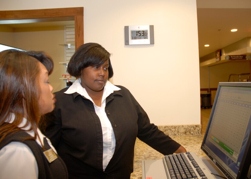 Adrienne Jackson, Commando Inn guest services employee, receives traning from Benjamas Miller, Commando Inn accounting clerk, on the computer systems at the new lodging facility March 30.  More than 60 additional employees were hired to help staff the new facility, which opened March 28.(U.S. Air Force photo by Senior Airman Ryan Whitney)