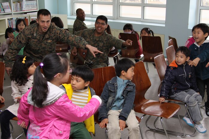 Yechon Air Base, REPUBLIC OF KOREA - Lance Cpl. Victor Contreras, a Foal Eagle participant, and Lt. Anthony Baker, Marine Wing Support Squadron 171 chaplain, encourage a girl to run and take the last open seat during a game of musical chairs at the Yechon Elementary School March 31. Several Marines and sailors visited the school to interact with the Korean children to improve community relations.