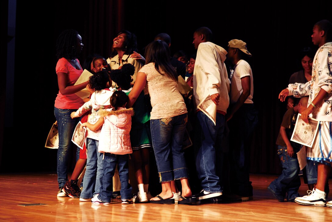 Dana Nelson, author and founder of Youth Expressions, a youth group focusing on the performing arts, receives a group hug from the group’s members at the end of their second play, “Second Chance,” at the community center on Camp Foster May 1. Youth Expressions gives youth the opportunity to express themselves through writing, poetry, acting, dance and singing.