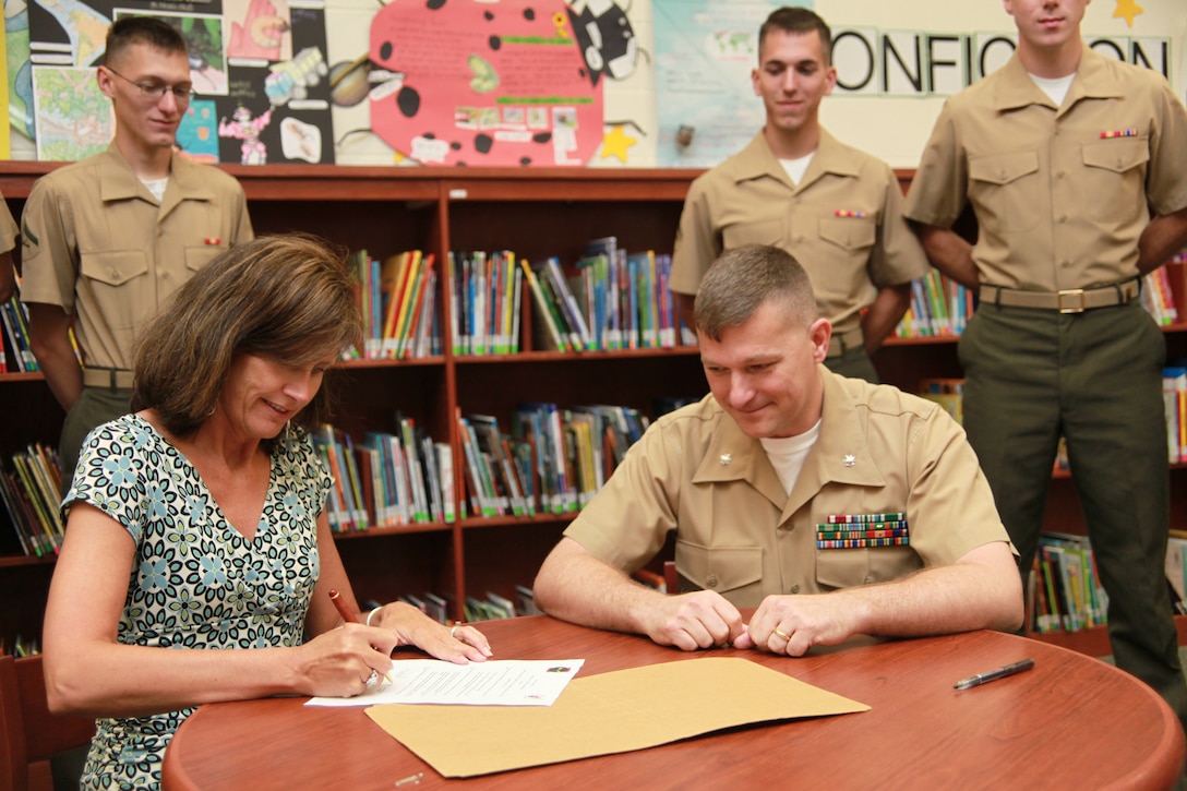 Abbey Whitford, principal of Creekside Elementary School in New Bern, N.C., and Lt. Col. Chris S. Richie, commanding officer of Marine Air Control Squadron 2, sign an agreement to adopt Creekside Elementary School as part of a volunteer program, May 3.