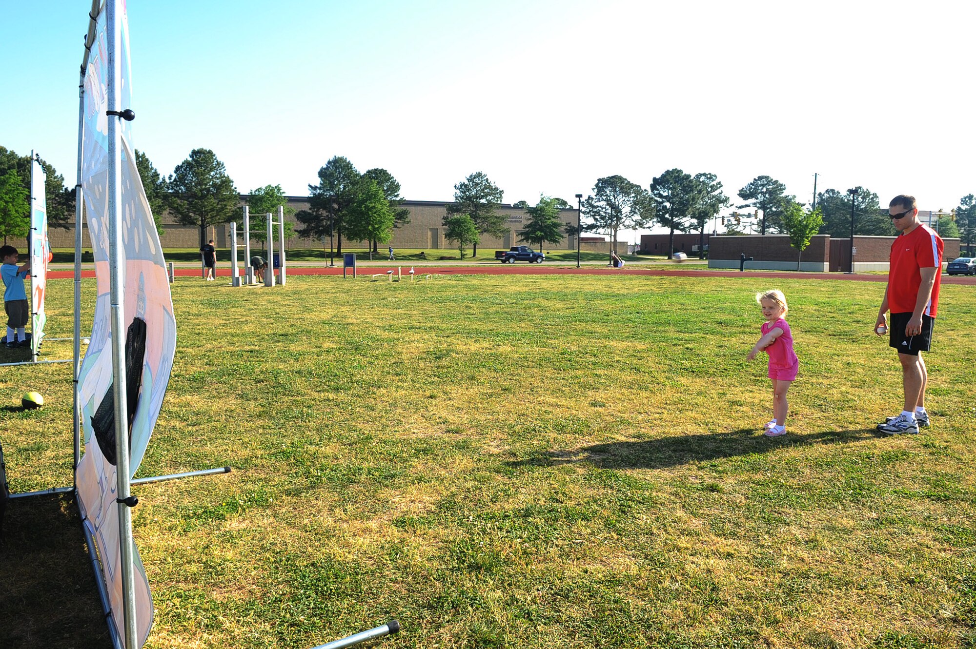 LANGLEY AIR FORCE BASE, Va. -- Staff Sgt. Alex Johnson, 1st Aircraft Maintenance Squadron, helps his daughter, Briana throw a baseball into the catcher's hand during the kick-off extravaganza of May fitness month at the shellbank fitness center track May 1. The annual event is all month long, which is in conjunction with The Year of the Air Force Family this year,  motivating Air Force personnel and their families to get up, get out, and get fit together. (U.S. Air Force photo/Staff Sgt. Ashley Hawkins)