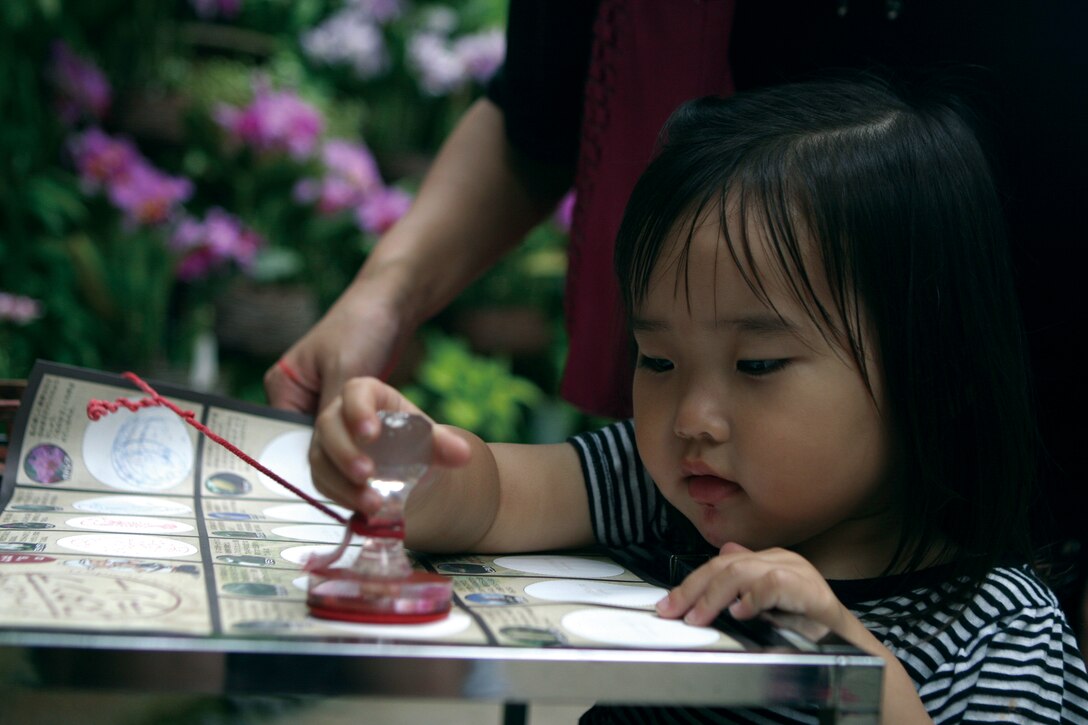 Luna Morita, a 2-year-old visitor to the Tropical Dream Center in Motobu, stamps her tour card at one of the stamping stations set up along the tour route.
