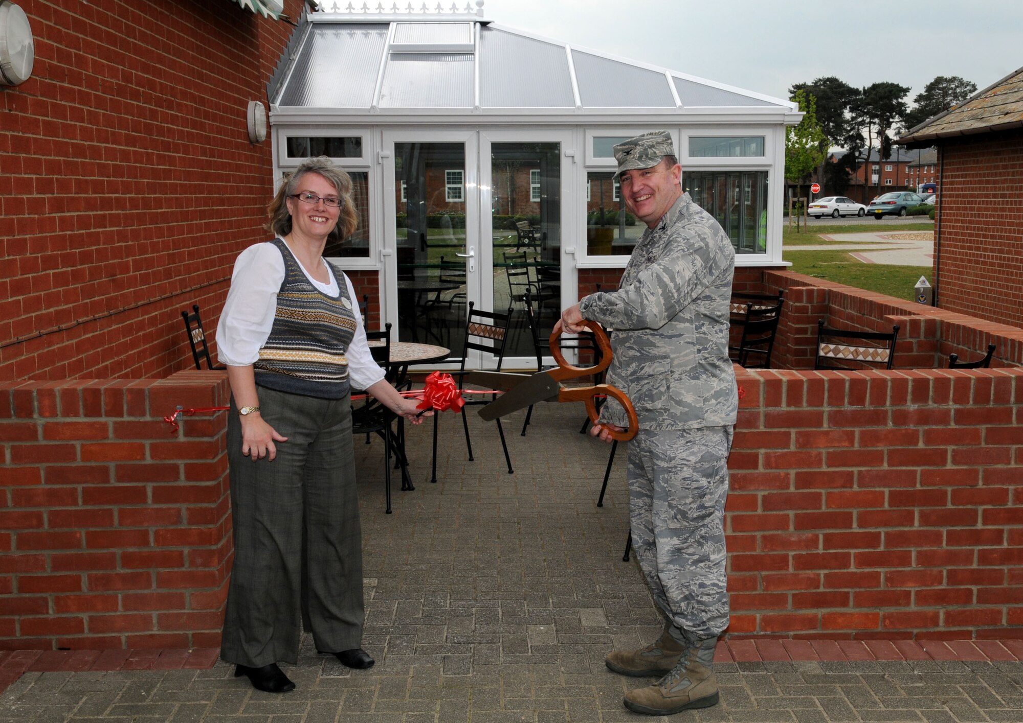 RAF MILDENHALL, England – Col. Jeffery Bateman, 100th Mission Support Group commander, and Stephanie Lown, community center director, perform the ribbon cutting ceremony for the newest addition at the Bob Hope Community Center during the conservatory grand opening May 6. The English garden offers an outdoor sitting area with Wi-Fi accessibility and a conservatory in case of inclement weather and for open viewing. (U.S. Air Force photo/ Staff Sgt. Jerry Fleshman)