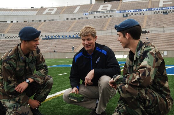 Cadets 1st Class Caleb Becker (left) and Ben Saunders discuss field conditions with Mike Wehrmann, Falcon Stadium manager. Here, the three examine a cross section of the artificial turf on the field. The cadets? research project found that the heating system that mitigates ice from the field before game time only needs to be turned on for 24 hours as opposed to a week before a cold weather game. 