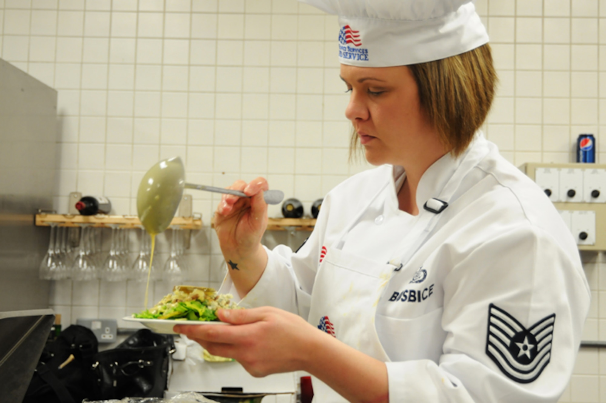 Tech. Sgt. Lindsey Busbice, Knight’s table blue team member, drizzles honey mustard vinaigrette onto a fruit salad during the second annual Hell’s kitchen cook-off at the Liberty Club at RAF Lakenheath, England, April 24. Sergeant Busbice was part of the military chefs who competed against civilian chefs from the Liberty Club. Each team created a gourmet menu of their own and were judged by designated judges, customers and mystery judges. With something to prove from last year’s defeat, the military chefs took home the victory this year. (U.S. Air Force photo by Airman 1st Class Lausanne Morgan)