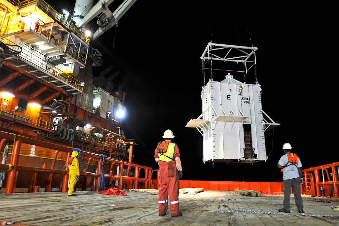 Crewmen aboard the motor vessel Joe Griffin look on as the mobile offshore drilling unit Q4000 lowers a pollution containment chamber, Gulf of Mexico, May 6, 2010. The chamber was designed to cap the oil discharge that was a result of the Deepwater Horizon incident.