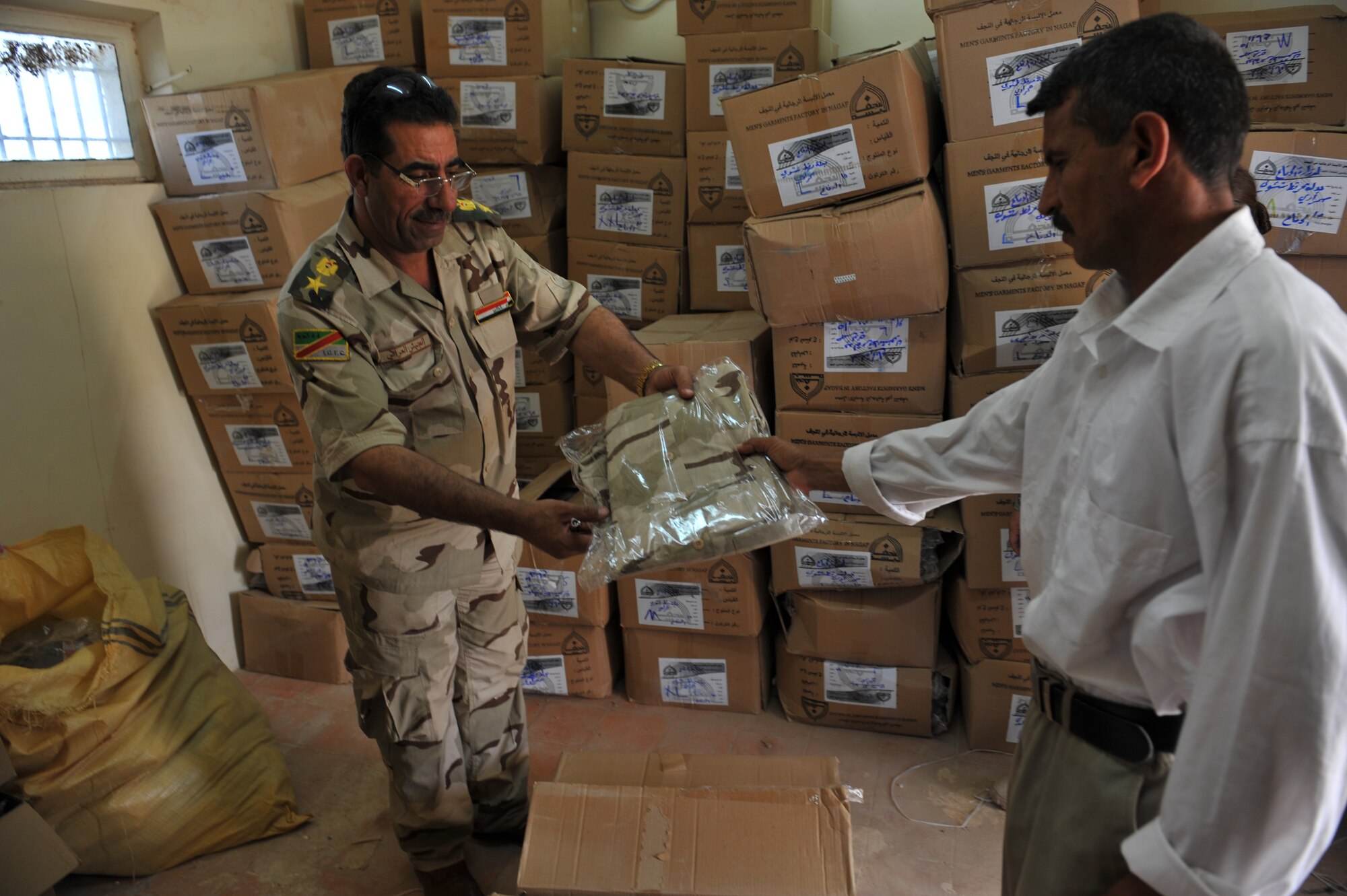 Iraqi Air Force Training School BMT Director Lt. Col. Ali Hussein Muhaimeed hands military uniforms to an Iraqi recruit at the Iraqi Air Force Training School, Camp Taji, Iraq, April 19, 2010. The Iraqi airmen volunteered to return to active duty through the rehire program by the Ministry of Defense.  (U.S. Air Force photo/Staff Sgt Quinton Russ/released)