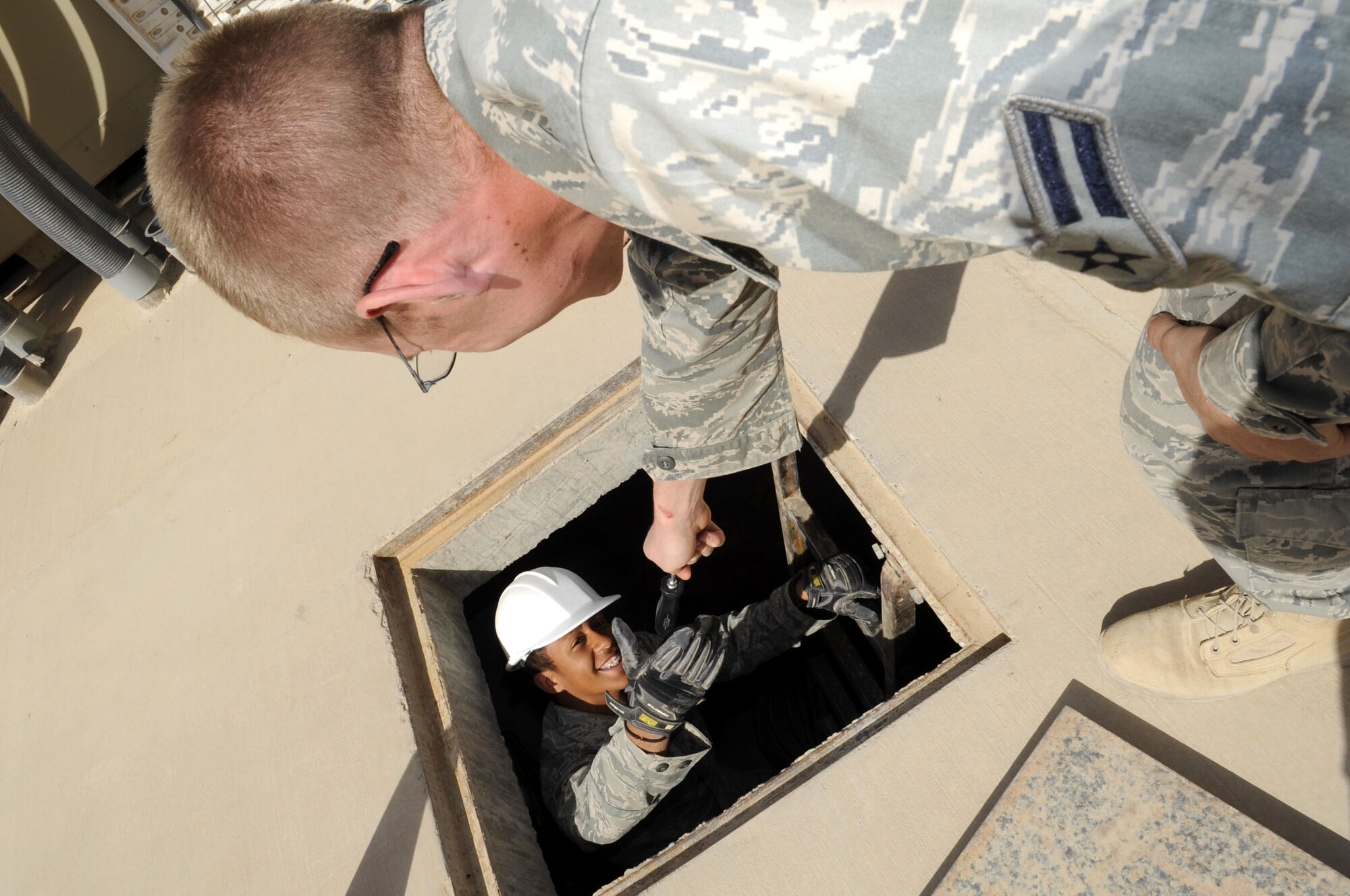Senior Airman Andre Vinning, left, and Airman 1st Class Ehren Brown, go inside a manhole to inspect tele-phone connectivity equipment. Members of the 451st Expeditionary Communications Squadron cable sys-tems, network infrastructure, cyber surety, radio and satellite systems work centers teamed up to provide communications support to Air Force units located at Camp Bastion. The project has been ongoing since December 2009. (U.S. Air Force photo by Senior Airman Nancy Hooks/Released)