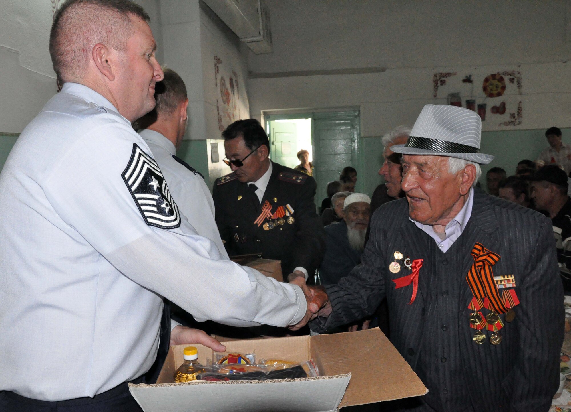 U.S. Air Force Command Chief Master Sgt. James Dowell, the enlisted leader for the Transit Center at Manas, Kyrgyzstan (left), shakes hands with a veteran of the Great Patriotic War (WWII) and presents him and five other veterans with boxes of food and basic dry goods after a Victory Day ceremony in Manas Village May 9, 2010. The mayor invited him and Col. Blaine Holt, the director of the Transit Center, to participate in the event, which honored living veterans and members of Manas Village who gave their lives during the Great Patriotic War (WWII). (U.S. Air Force photo/Staff Sgt. Carolyn Viss)