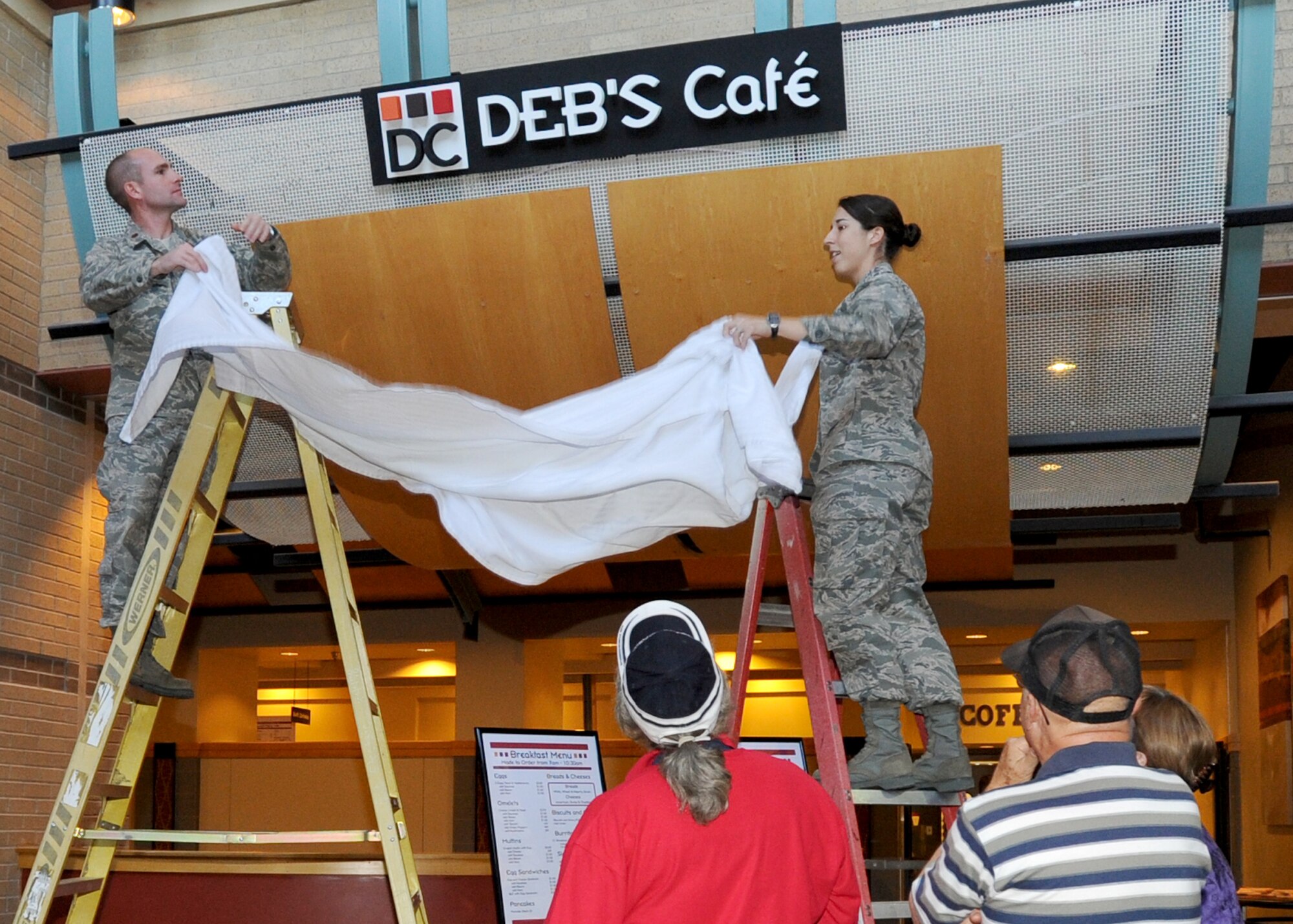 Maj. Colin Huckins, 22nd Force Support Squadron commander, and 1st Lt. Kelly Morrison, 22nd Force Support Squadron flight commander, uncover a sign during the grand re-opening of the newly relocated Deb’s Café May 6, 2010, McConnell Air Force Base, Kan. The new location now features a revamped menu, new coffee bar and free wireless internet.  Deb’s Café is now located inside the Robert J. Dole Community Center in what used to be the Rendezvous Café. (U.S. Air Force photo/Airman 1st Class Andrea Salazar)