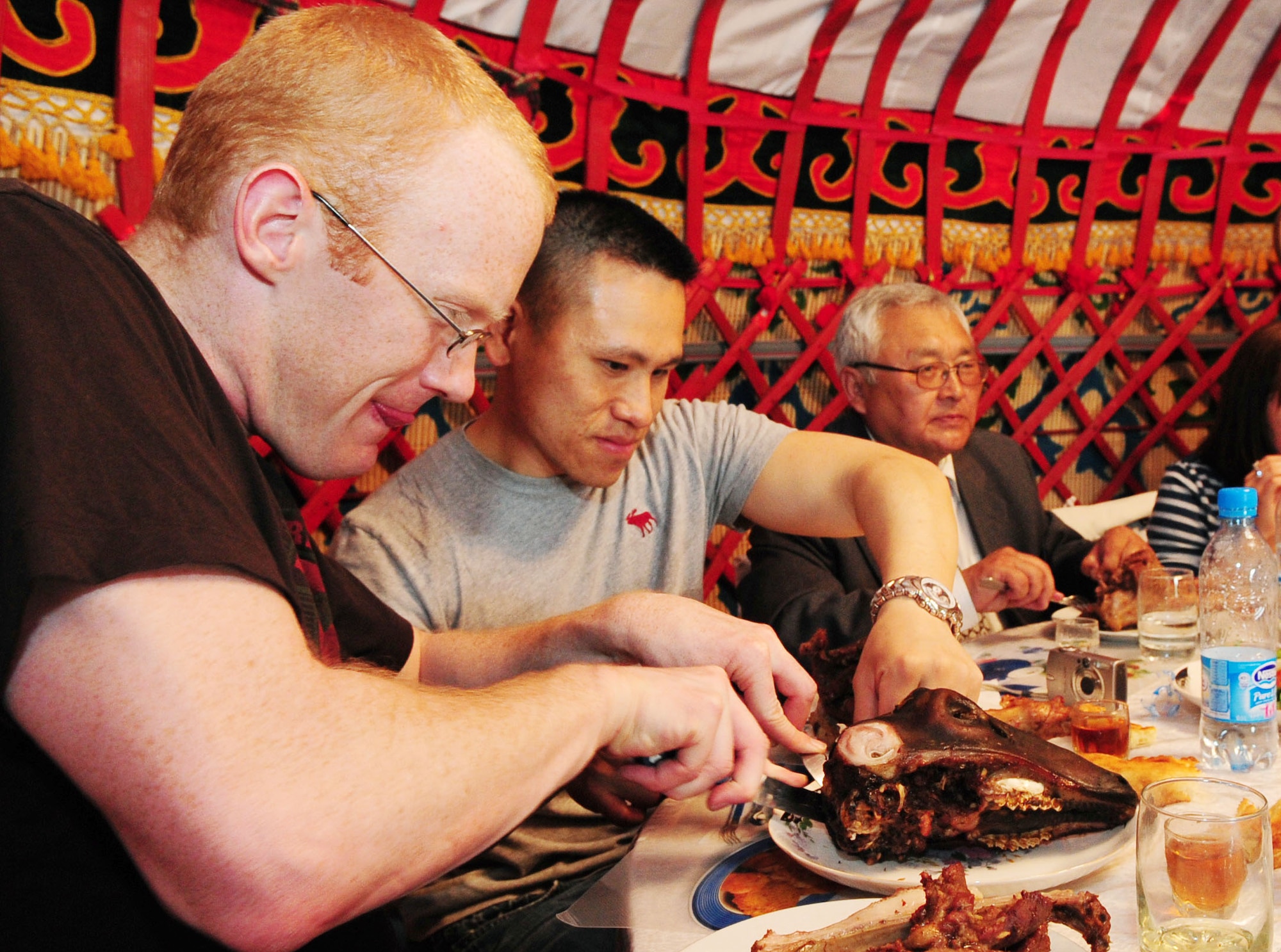 U.S. Air Force Captains Alan Yee and Andrew Washburn, 376th Air Expeditionary Wing executive officers, cut meat off a lamb's head during a Kyrgyz traditional hunter's barbeque near Bishkek, Kyrgyzstan, May 6, 2010. Airmen from the Transit Center at Manas were invited to participate where they enjoyed a variety of traditional food. In the Kyrgyz culture, the lamb's head is given to the most honored guest. (U.S. Air Force photo/ Senior Airman Nichelle Anderson/ released)