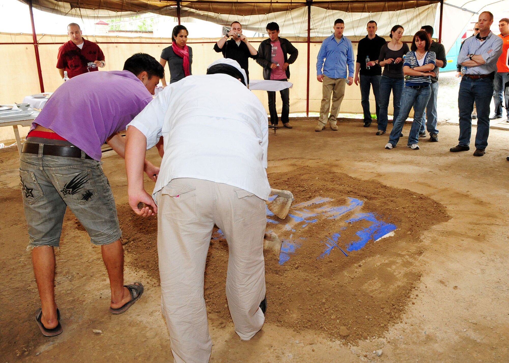 Airmen from the Transit Center at Manas, Kyrgyzstan, watch as cooks unveil the smoked lamb from an underground barbeque pit known as a tandyr, in Kyrgyz culture, in the center of a yurt May 6, 2010. The Airmen were invited to participate in a traditional Krygyz hunter's barbeque, where they enjoyed a variety of food. (U.S. Air Force photo/ Senior Airman Nichelle Anderson /released)