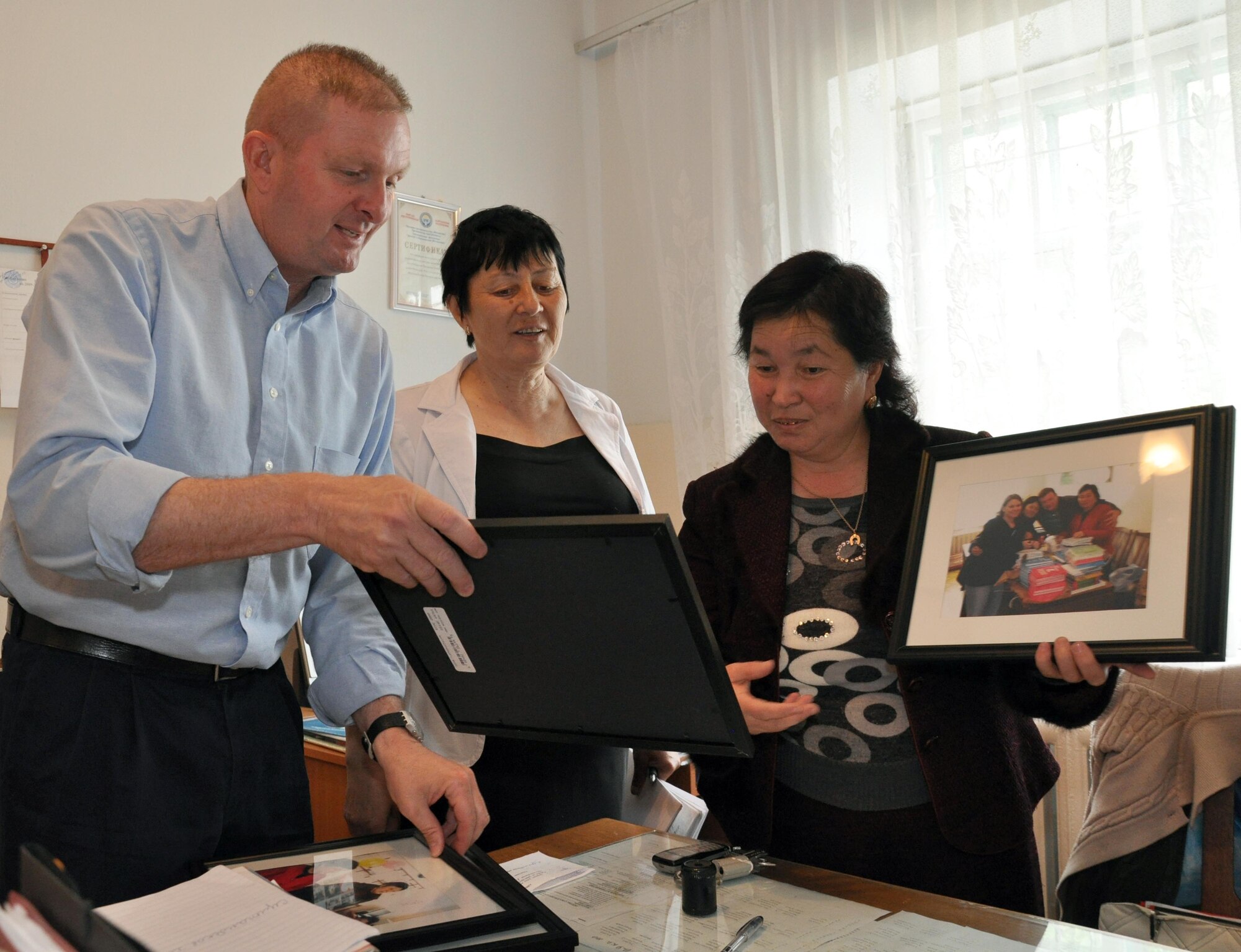 Command Chief Master Sgt. James Dowell, the enlisted leader of the Transit Center at Manas, Kyrgyzstan, presents framed photos of a previous visit from the Airmen at the Transit Center at Manas, to the director of Jany-Pakhta School through interpretation by Valentina Turabekova May 11, 2010. Jany-Pakhta Schools are sponsored by Manas Area Benefit Outreach Society, and Airmen visit regularly to play with children and give them textbooks and other items the schools need. (U.S. Air Force photo/Staff Sgt. Carolyn Viss)