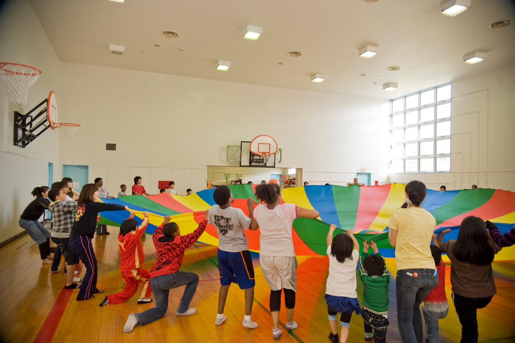 Children from Misawa Air Base’s Sollars Elementary School student council program and children from Japan’s Shichinohe Bikoh-En orphanage raise a parachute together during an activity in the school’s gymnasium, May 8, during a sport’s exchange event. The children played a variety of games and sporting events together, which lessened the language barrier between the groups. (U.S. Air Force/Senior Airman Jessica Lockoski)