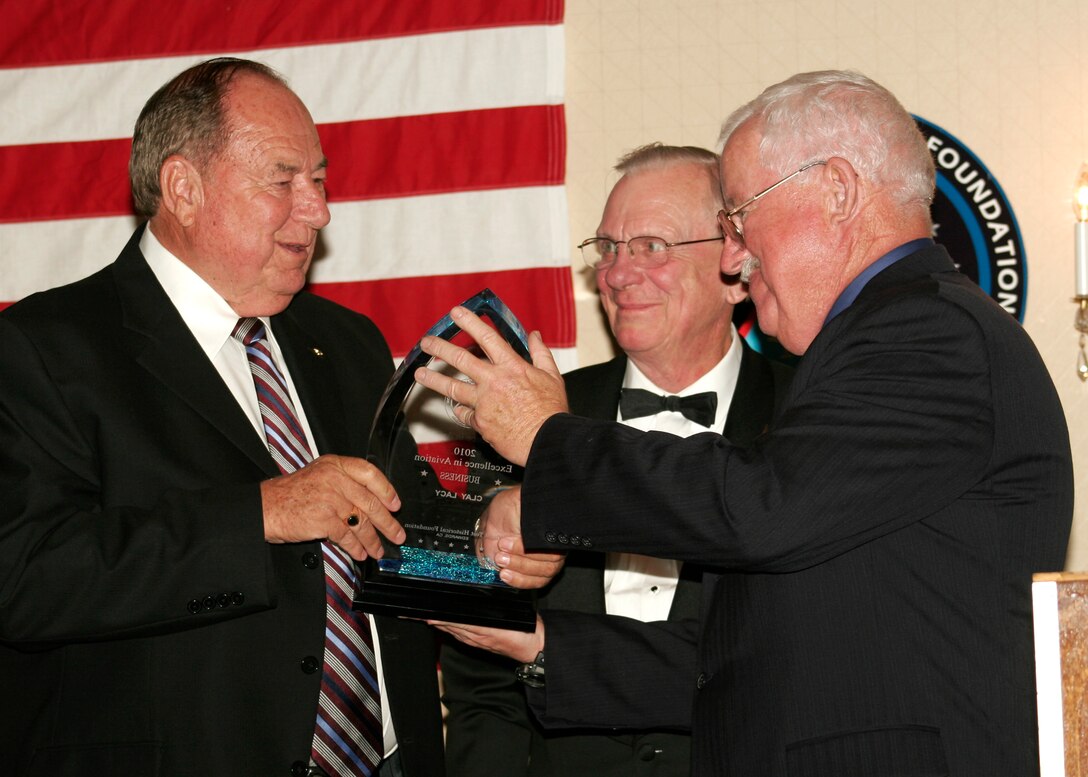 Clay Lacy (left) receives an Excellence in Aviation award presented by Flight Test Historical Foundation Chairman Bill Flanagan along with Master of Ceremony Ken Wolt (center). Mr. Lacy is a pilot and considered one of the top aerial cinematographers in the world. He has conducted more than 2 ,500 air-to-air photography flights, from Hollywood blockbusters to commercials for airlines. (Aerotech News photo by Linda KC Reynolds)