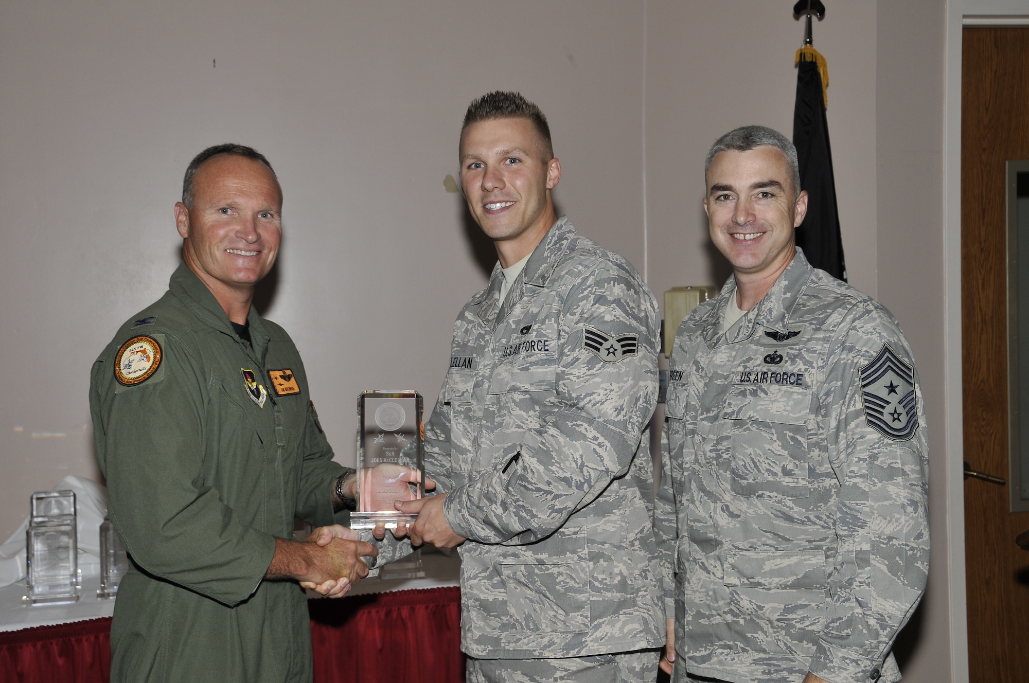 Colonel James Browne, 325th Fighter Wing commander, presents Senior Airman John McClellan, 325th Aircraft Maintenance Squadron F-22 avionics systems journeyman, the Tyndall Honor Guard member of the quarter award, as Chief Master Sgt. Jackie Greene, 325th FW command chief, looks on.