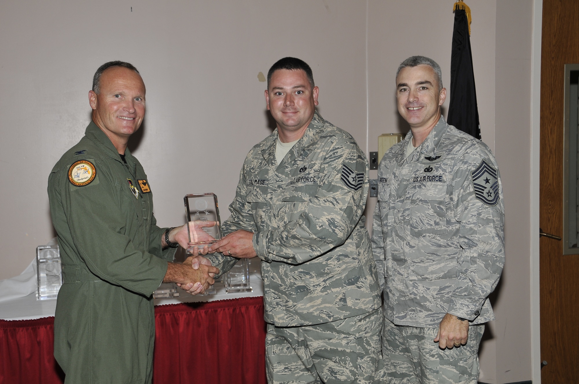 Colonel James Browne, 325th Fighter Wing commander, presents Technical Sergeant Lucky Talmage, AFCESA power generation specialist, the Associate Unit NCO of the Quarter award, as Chief Master Sgt. Jackie Greene, 325th FW command chief, looks on.