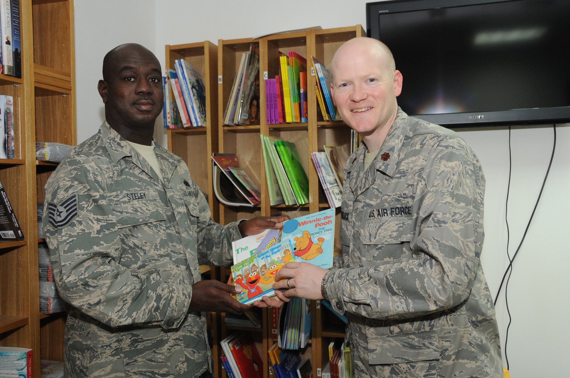 Tech. Sgt. Oswald Steley, Learning Resource Center manager for the 380th Expeditionary Force Support Squadron, and Maj. (Dr.) Kevin Bohnsack, 380th Expeditionary Medical Group, exchange books for the United Through Reading Program for the 380th Air Expeditionary Wing. The books were donated by the spouses group for the 64th and 65th Interceptor Squadron at Nellis Air Force Base, Nev. (U.S. Air Force Photo/Senior Airman Jenifer H. Calhoun)